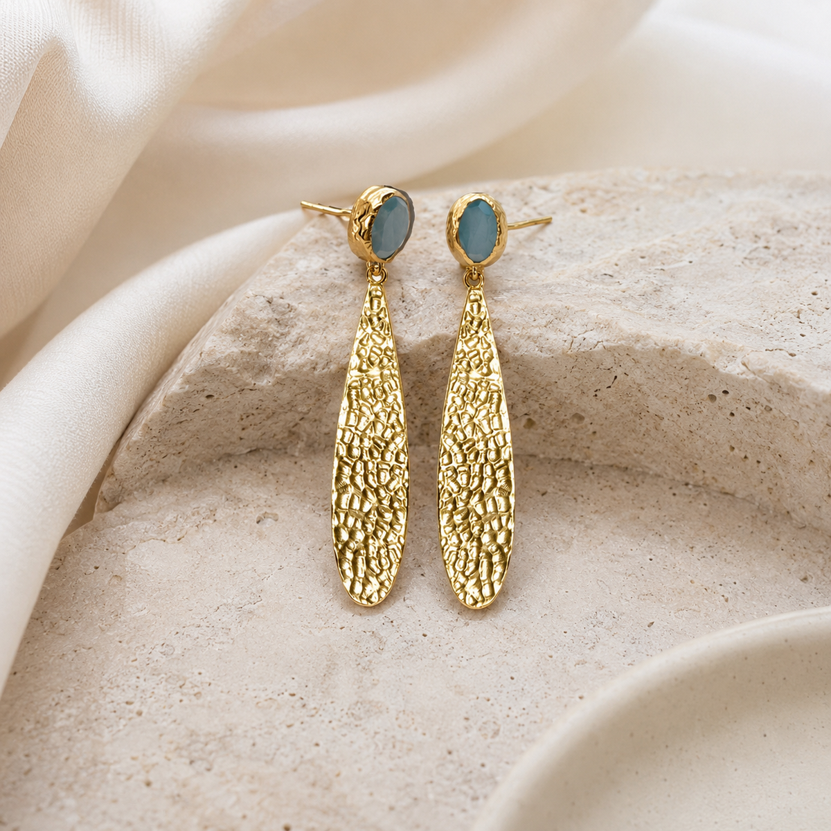 Hammered gold-plated drop earrings with a long textured silhouette and blue oval accents.