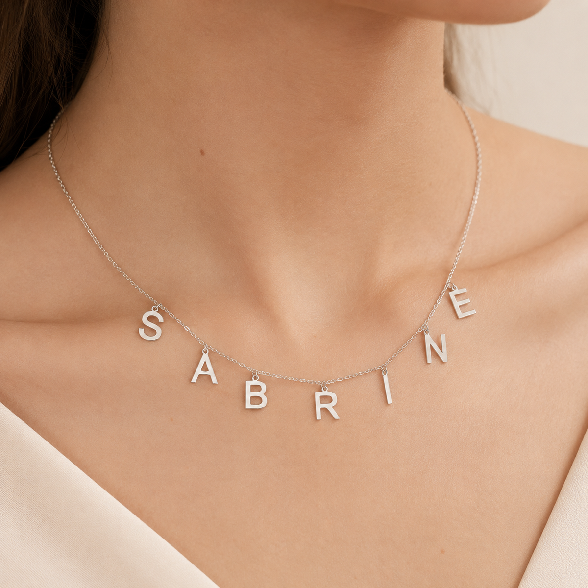 Silver-tone letter necklace styled flat with multiple initial charms along a fine chain.