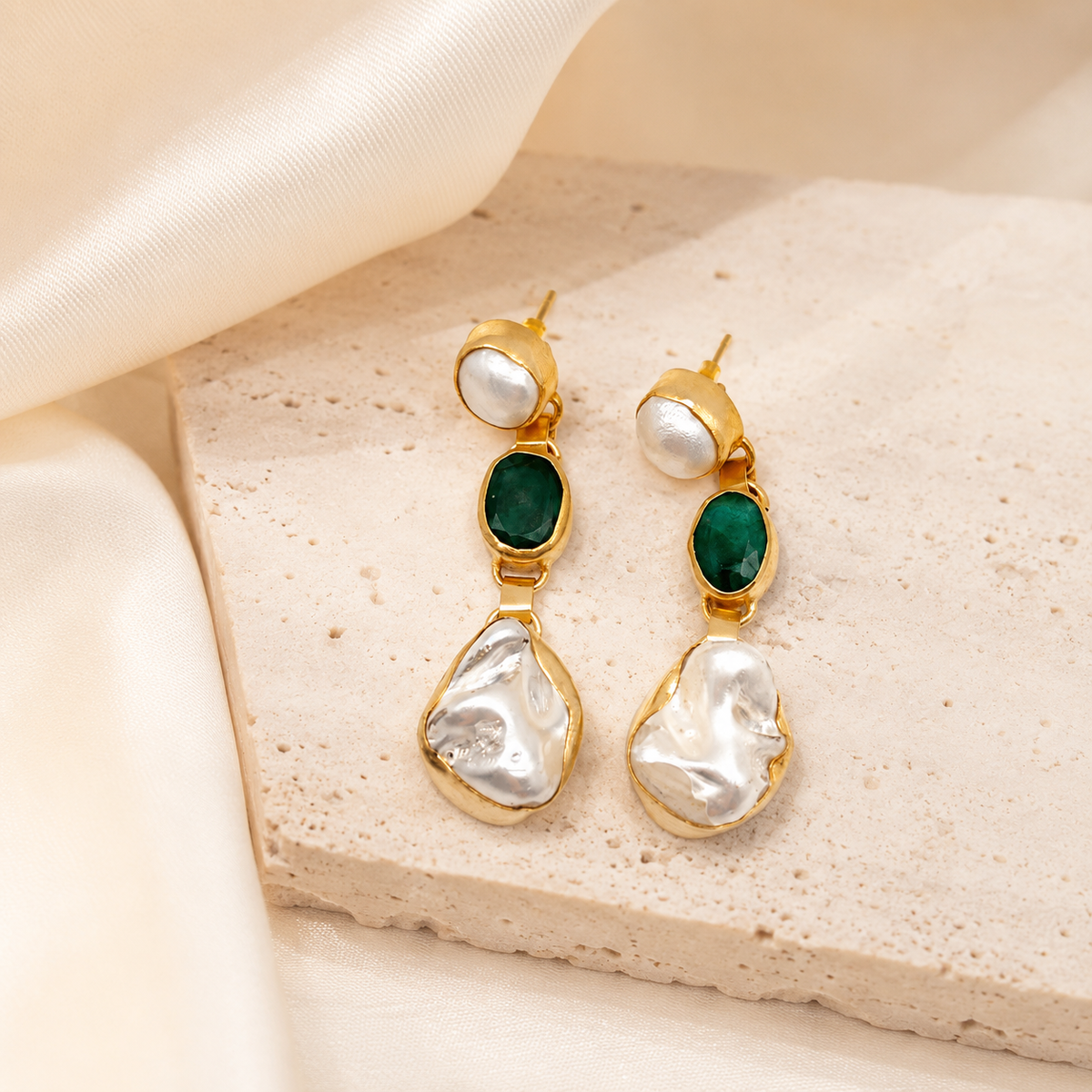 Gold drop earrings with emerald green accents and sculpted pearl-like drops on a white background.