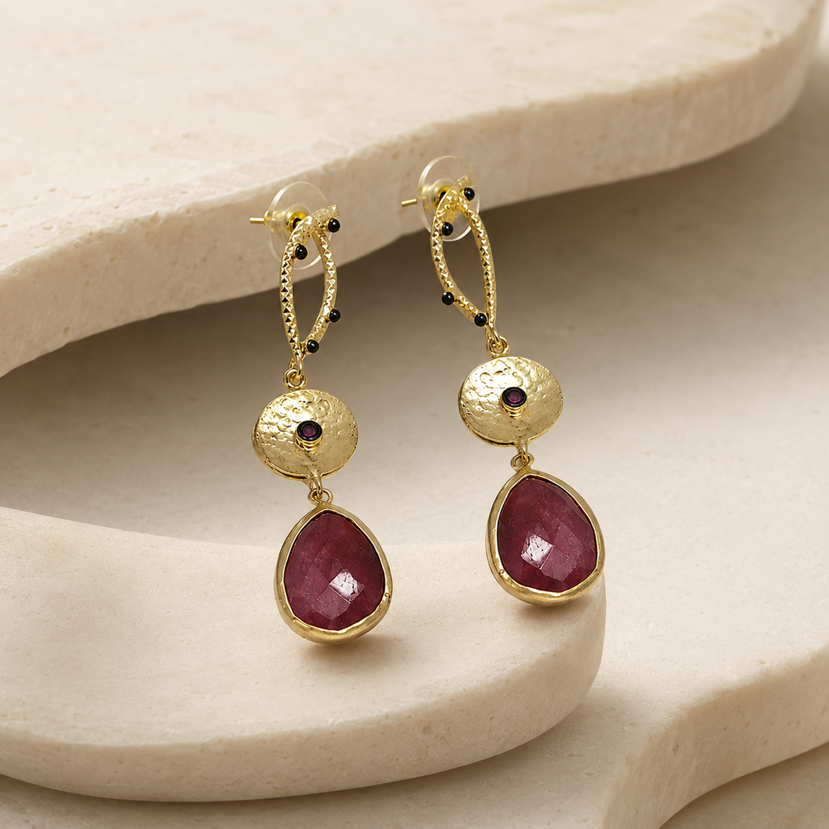 Angle view of long gold-plated statement earrings with textured gold links and red faceted drops.