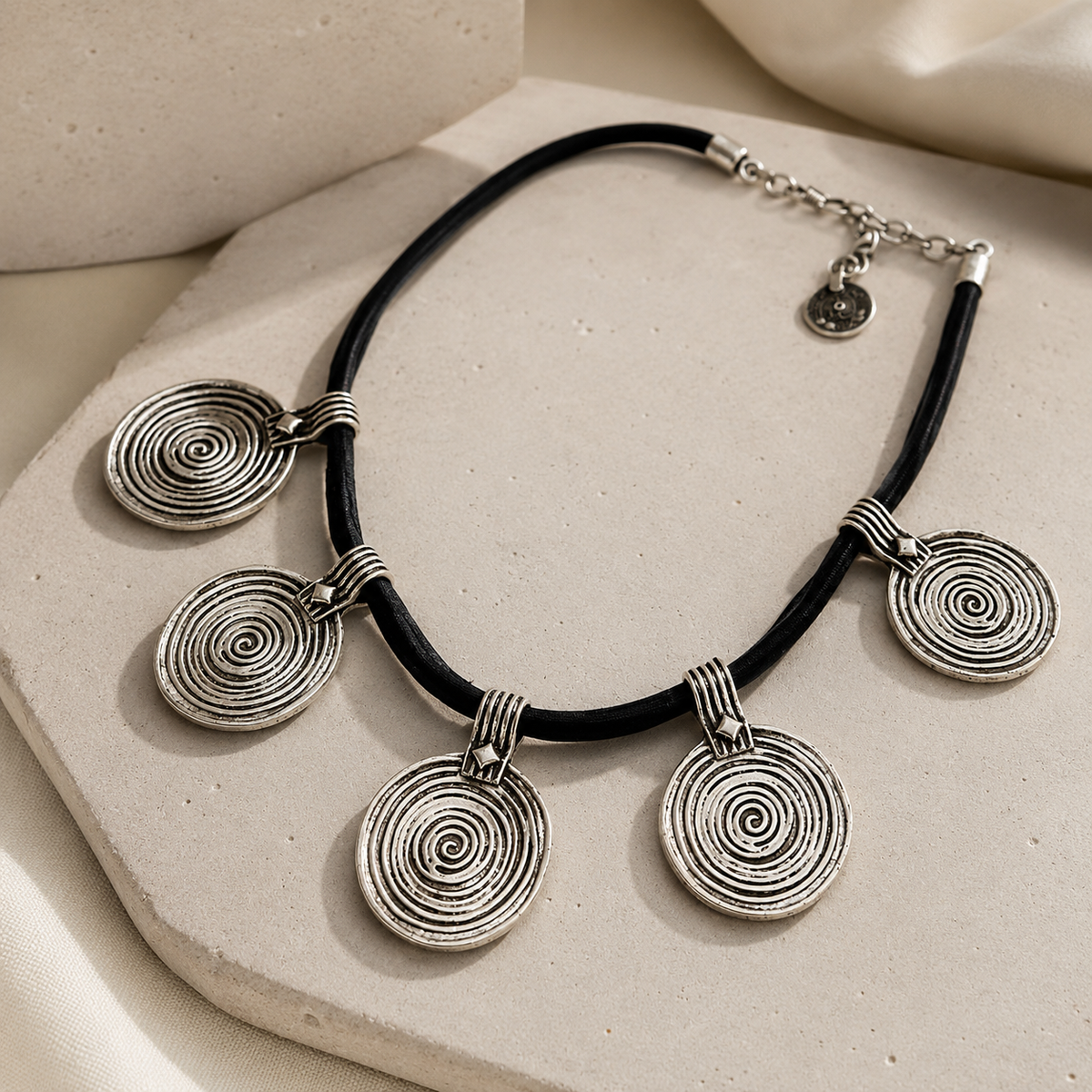 Angled view of a black cord necklace with spiral disc pendants.