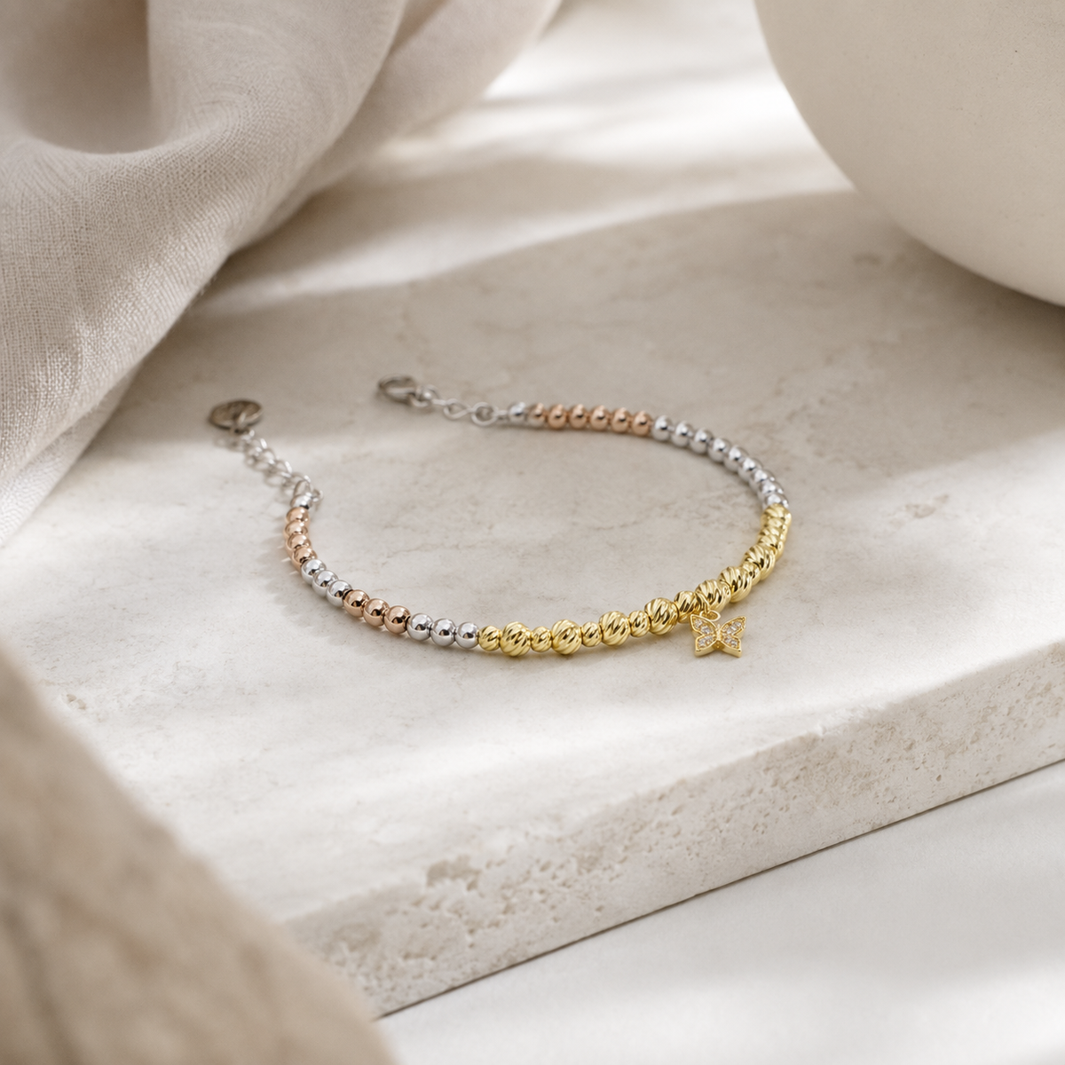 Angled view of a bracelet with mixed metallic beads and a butterfly charm.