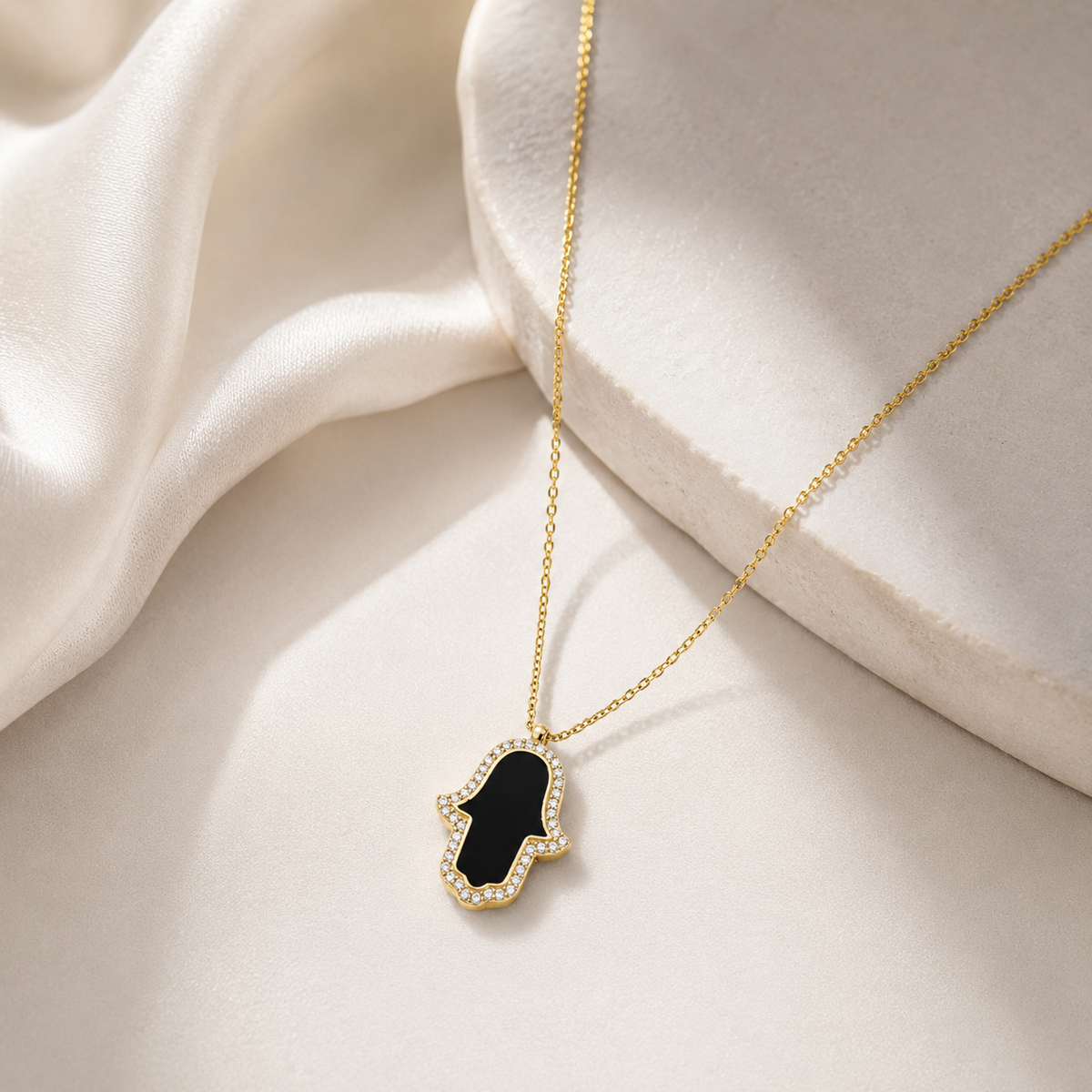 Minimal gold-tone necklace with a black hamsa pendant on a white background.