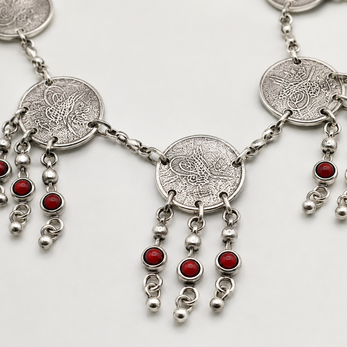 Close view of the textured coin discs and red bead fringe detail.