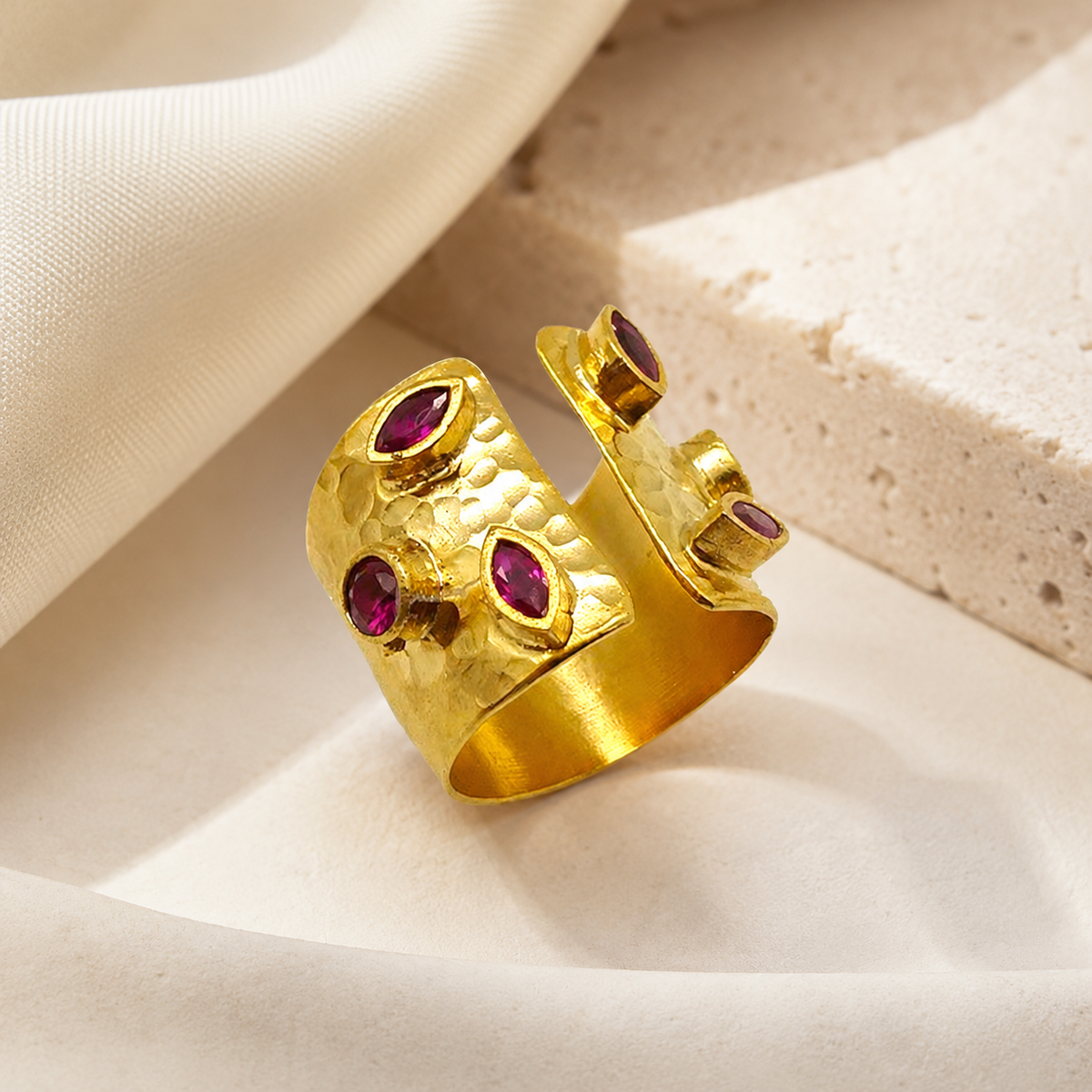Gold open cuff ring with cherry-toned stones on a white background.