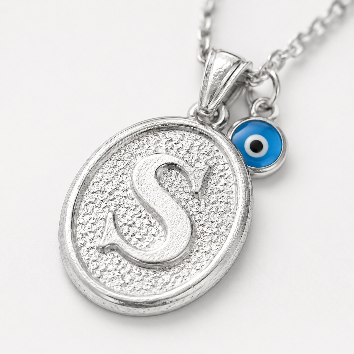 Close view of the oval initial pendant with a textured finish and small blue eye charm.