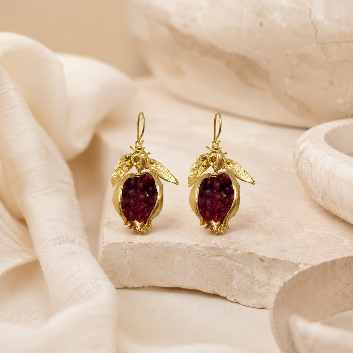 Gold drop earrings with pomegranate-red stones on a white background.