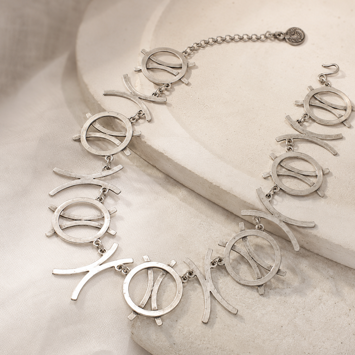 Silver-tone necklace with linked circle symbols and curved shapes on a white background.