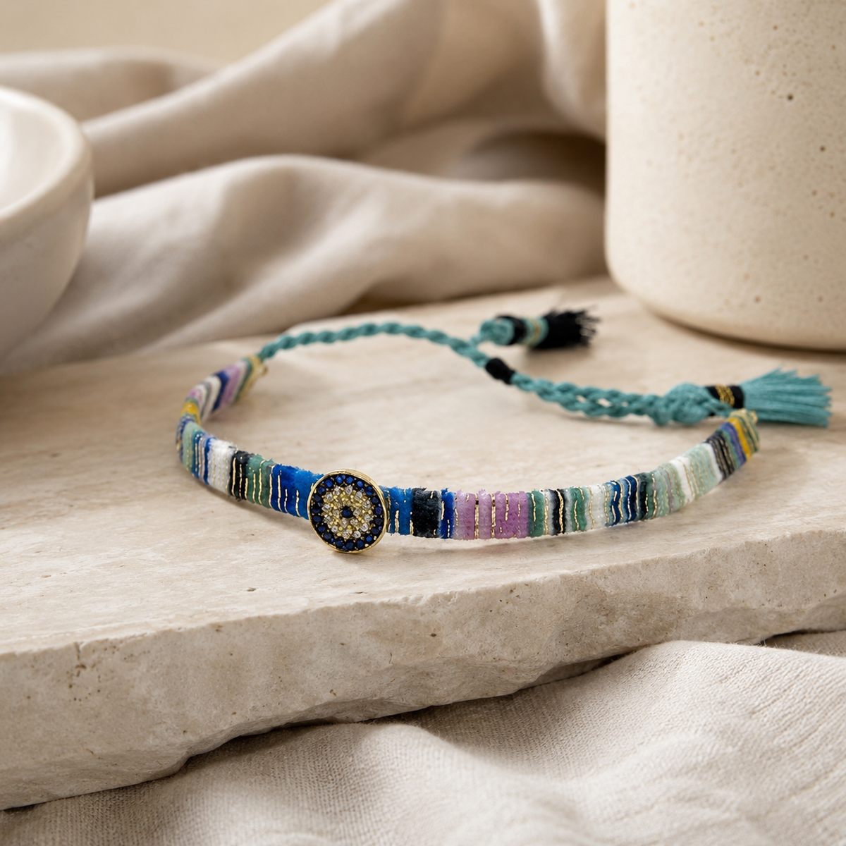 Angled view of a multicolor woven fabric bracelet with tassel ties and a jeweled center.