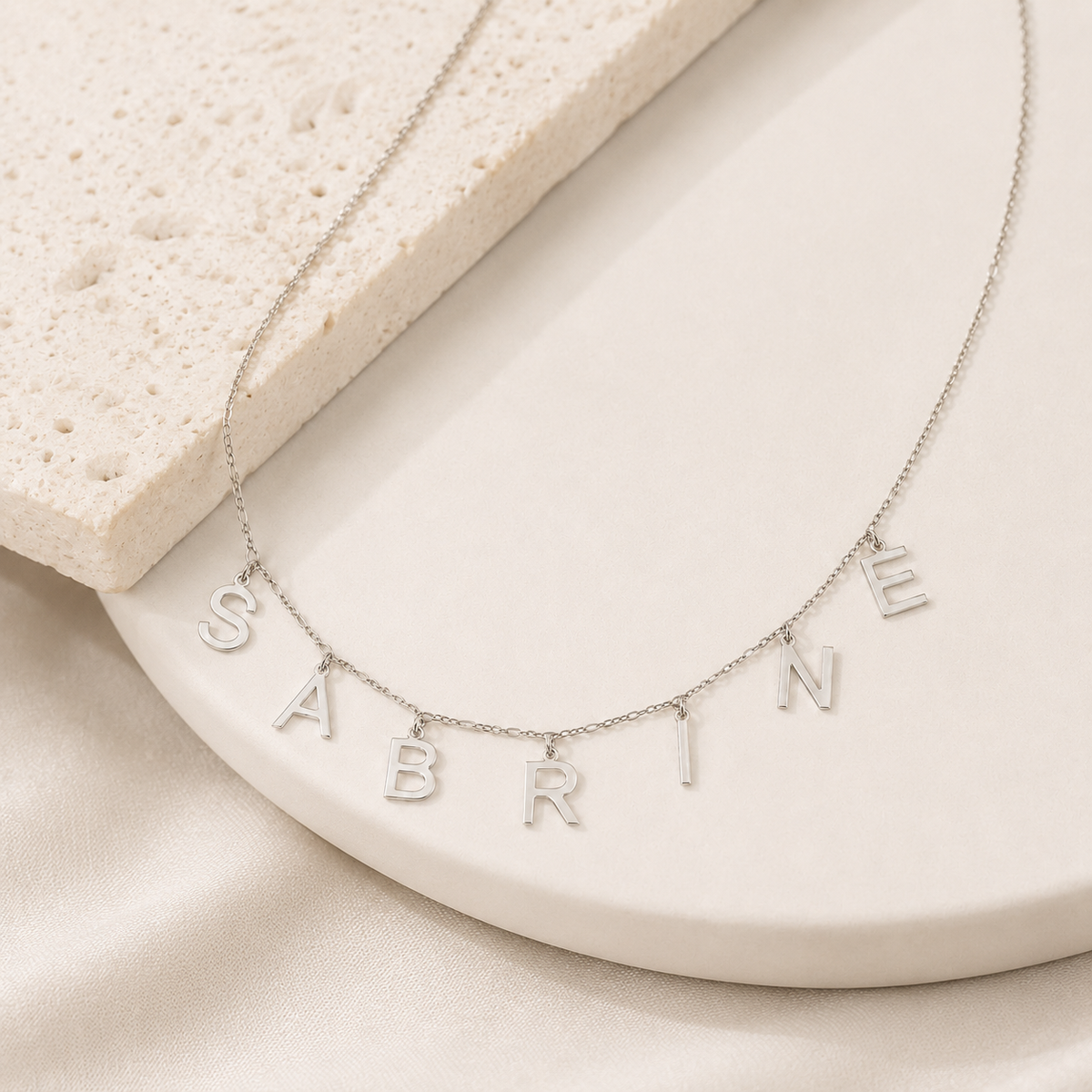 Angled view of a delicate personalized letter necklace with polished silver-tone charms.