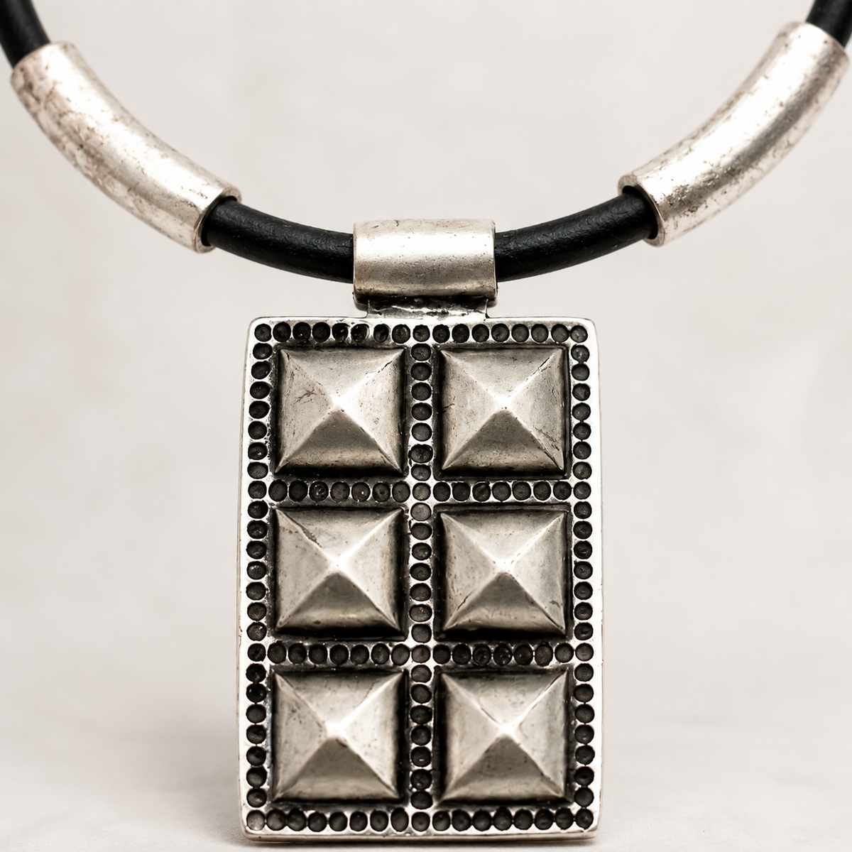 Close view of the geometric pendant and silver-tone accents on the black cord necklace.