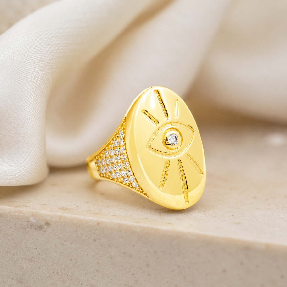 Gold-tone signet ring with an evil eye motif and bright accent.