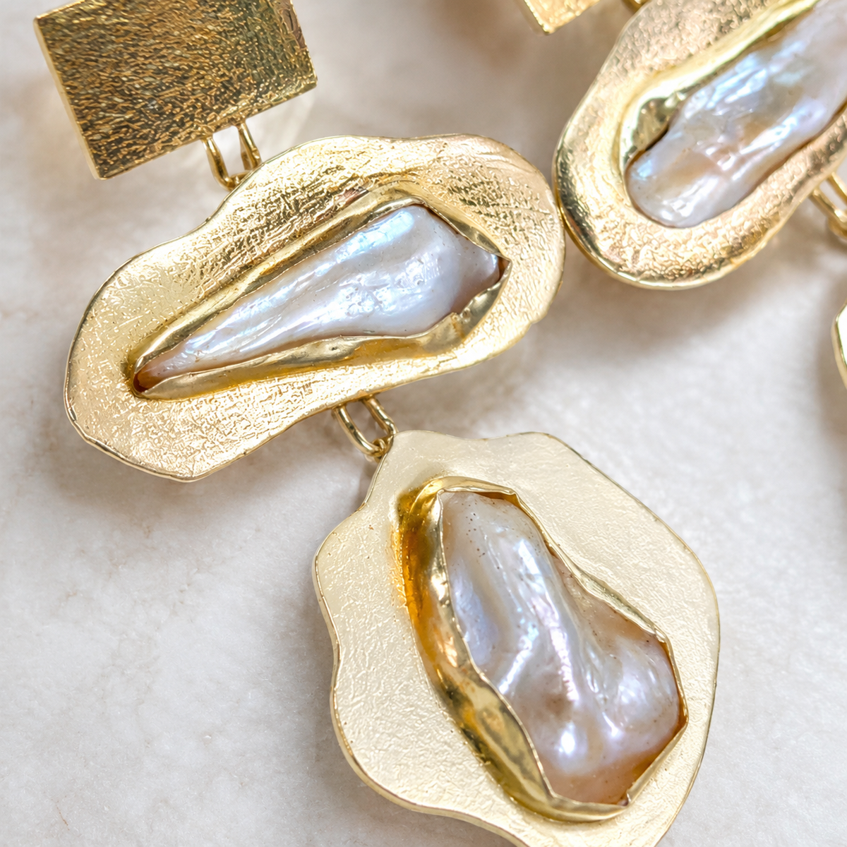 Close view of baroque pearl earrings with textured gold-plated detailing.