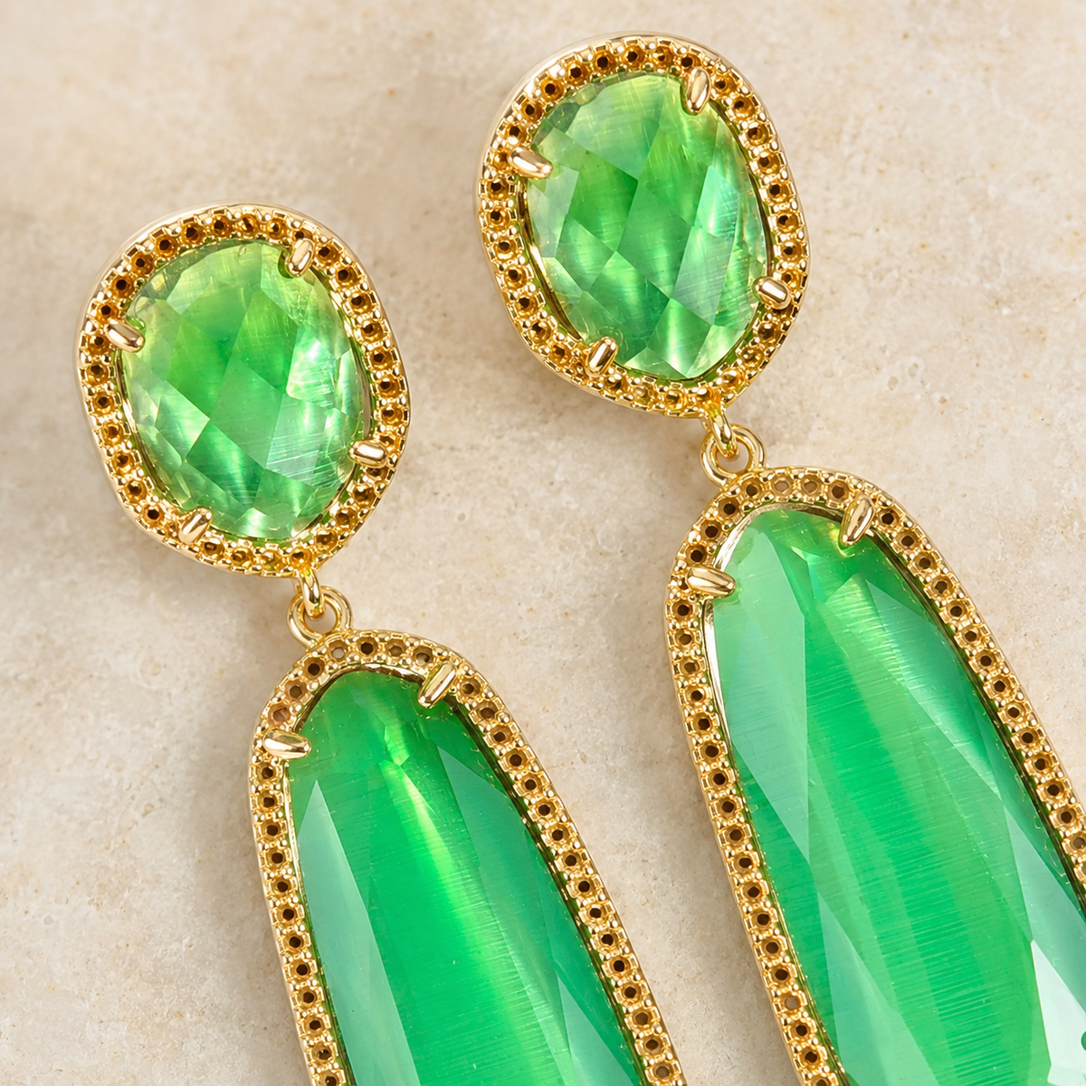 Close view of green faceted stones set in gold-plated earrings.