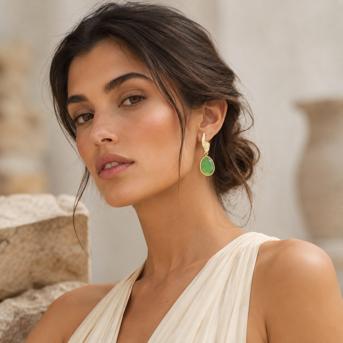 Pair of long drop earrings with bright green stones and textured gold-plated details.