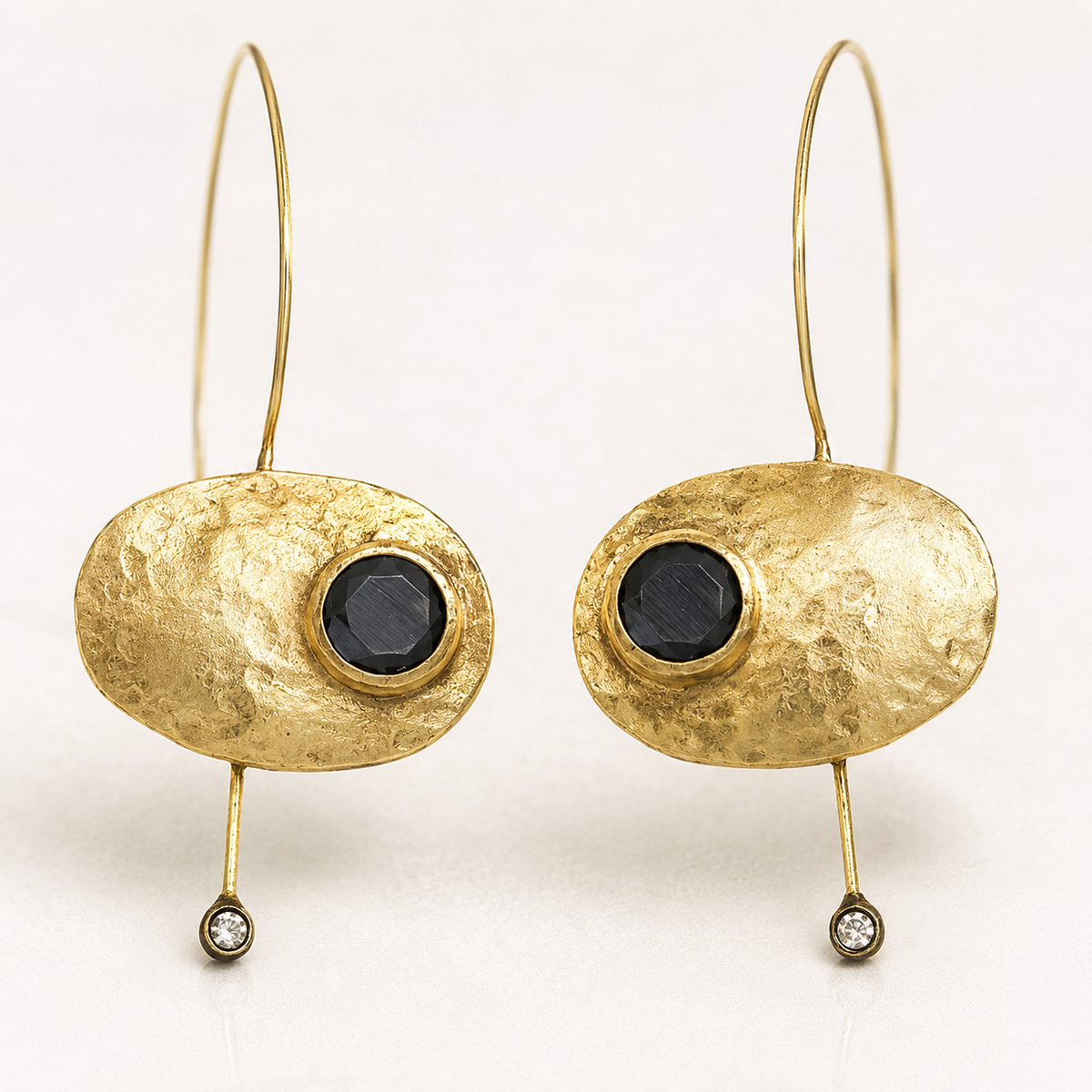 Close view of textured gold-plated earrings with black stone accents.