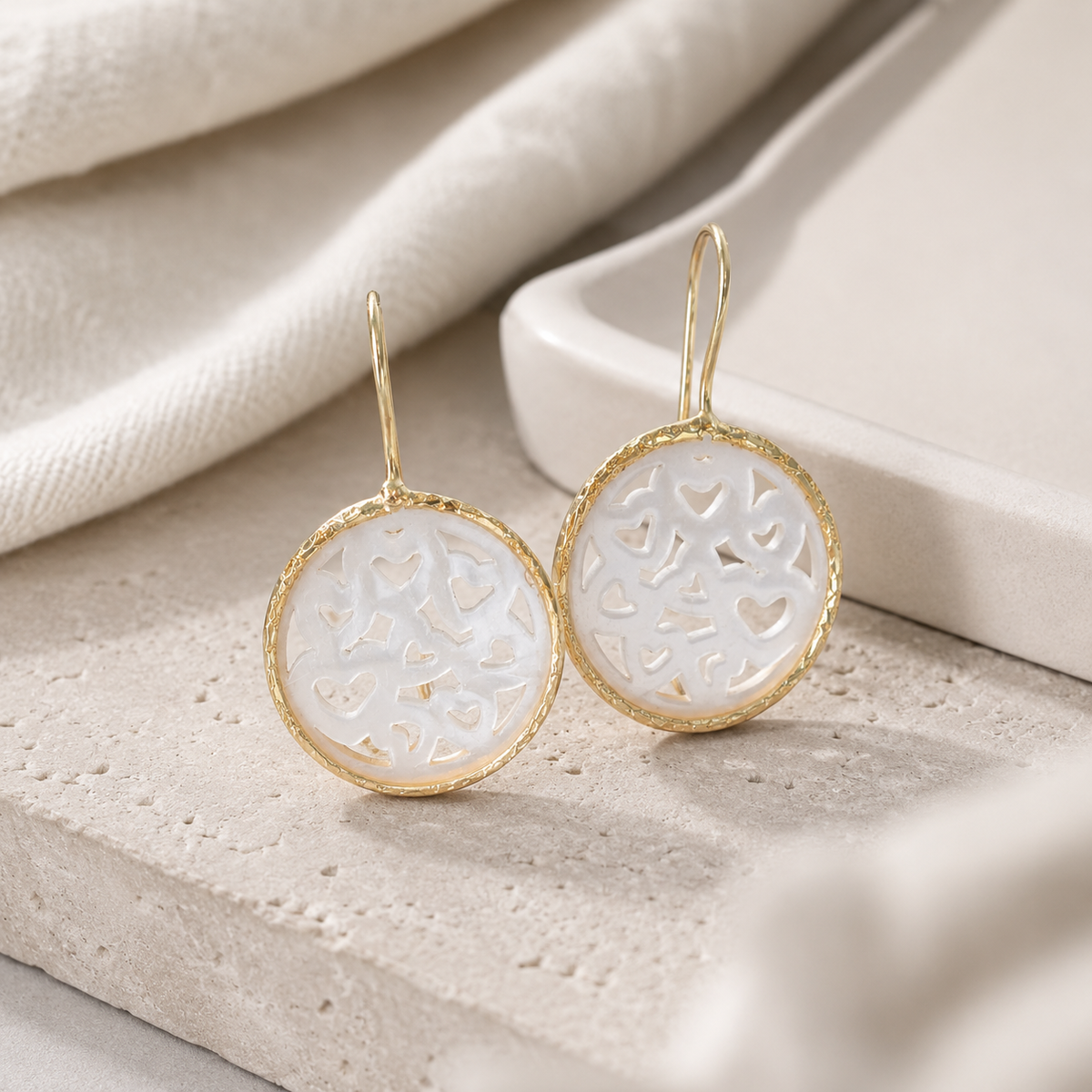 Angled view of gold-plated drop earrings with mother of pearl heart cutouts.