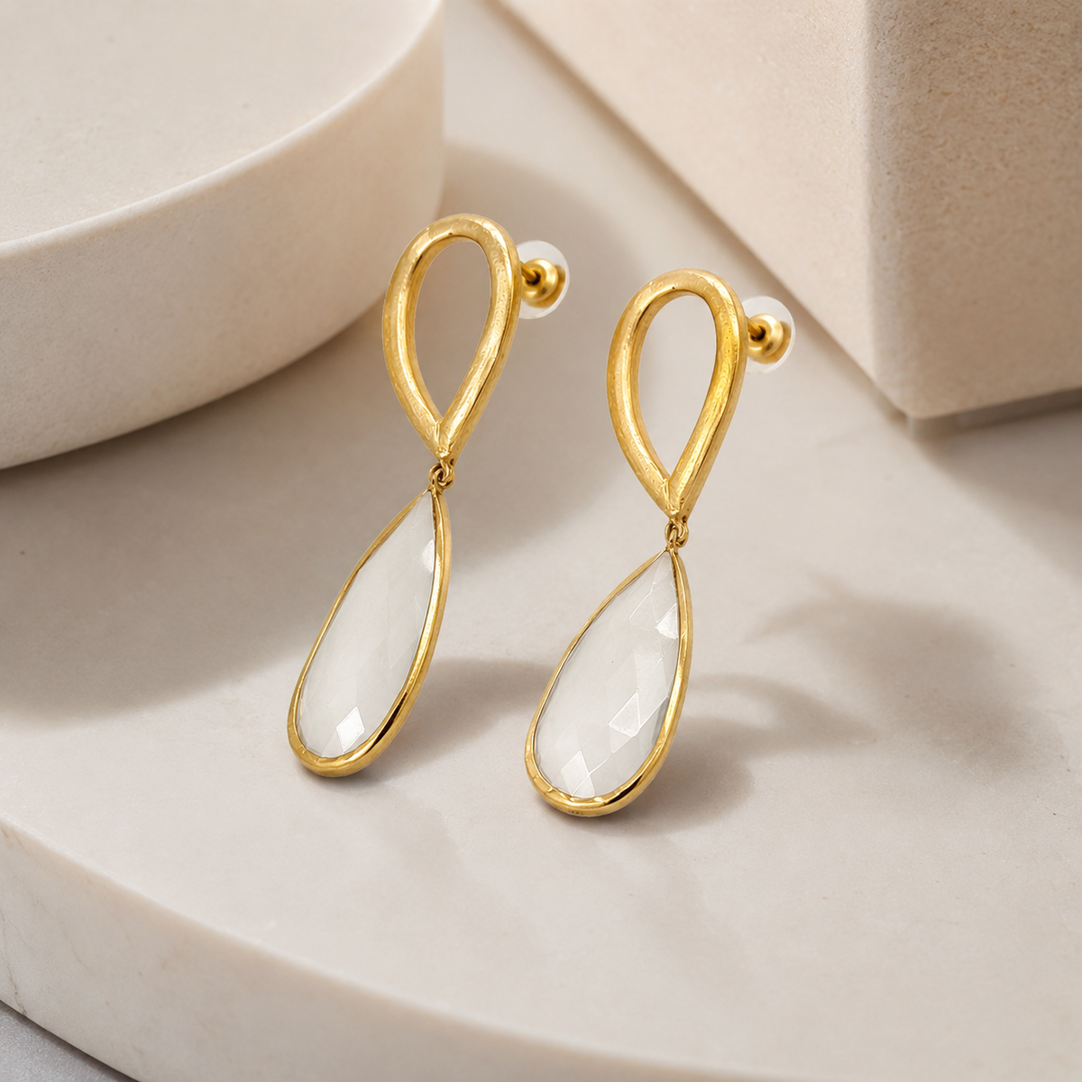 Angle view of hammered gold-plated drop earrings with clear teardrop accents.