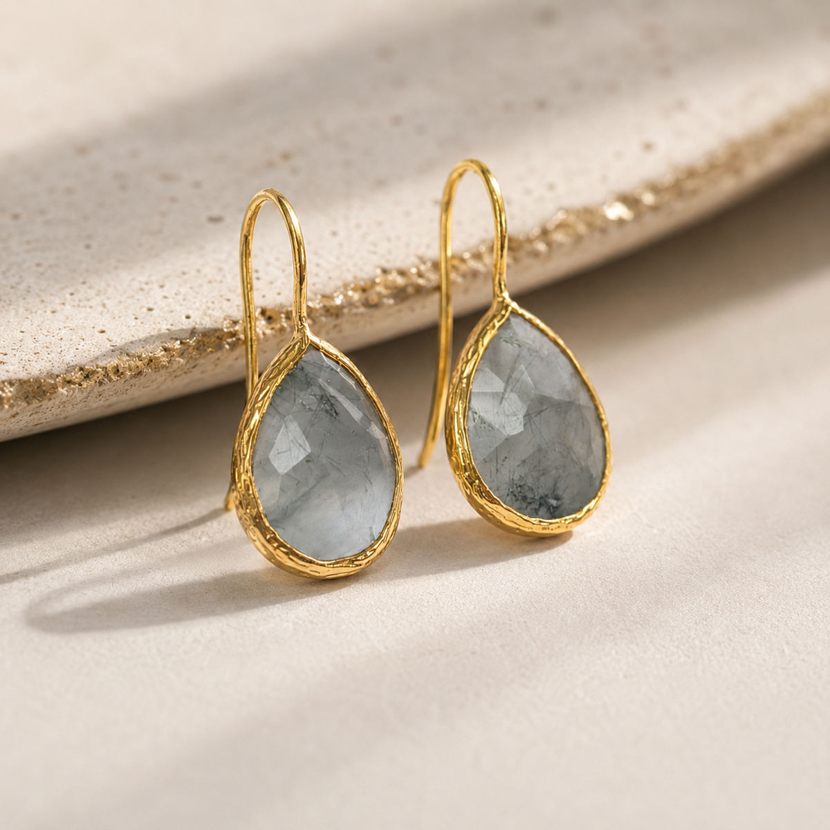 Angled view of teardrop earrings with faceted gray stones and gold-plated frames.