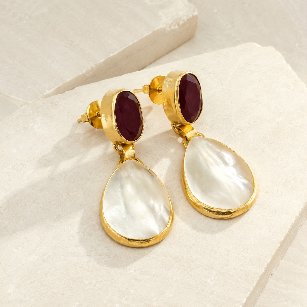 Front view of gold-plated drop earrings with red garnet and mother of pearl details.