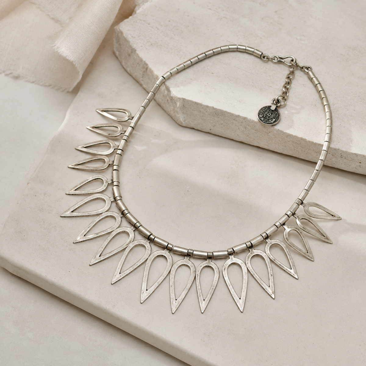 Angled view of a silver-tone teardrop collar necklace with a bold, open design.