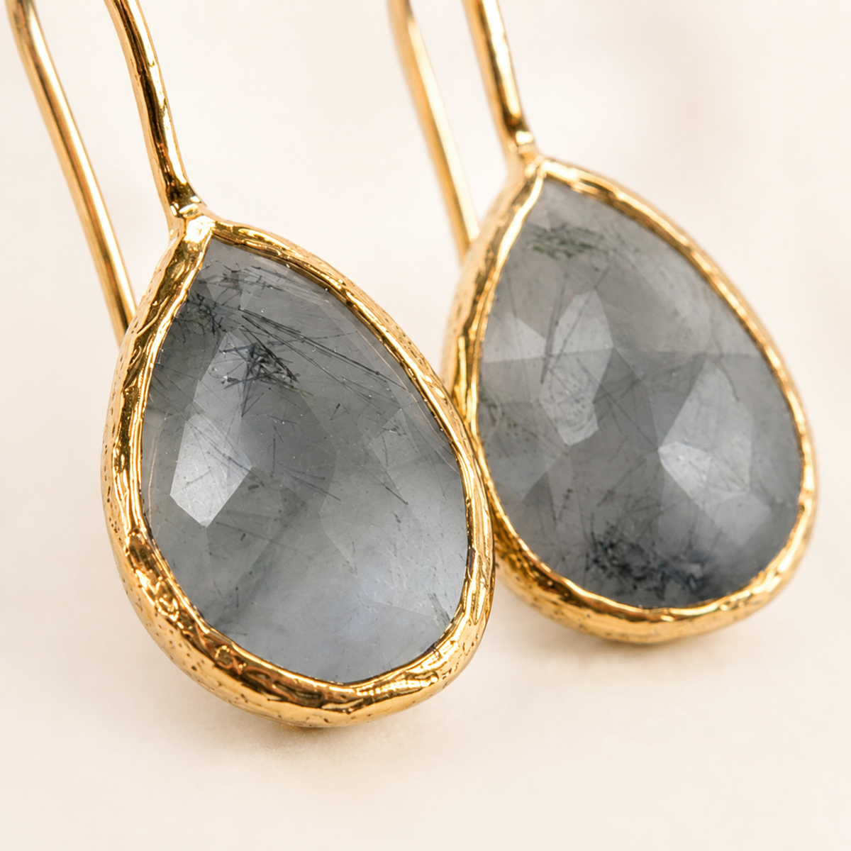 Close view of teardrop earrings showing faceted stone texture and gold-plated edges.
