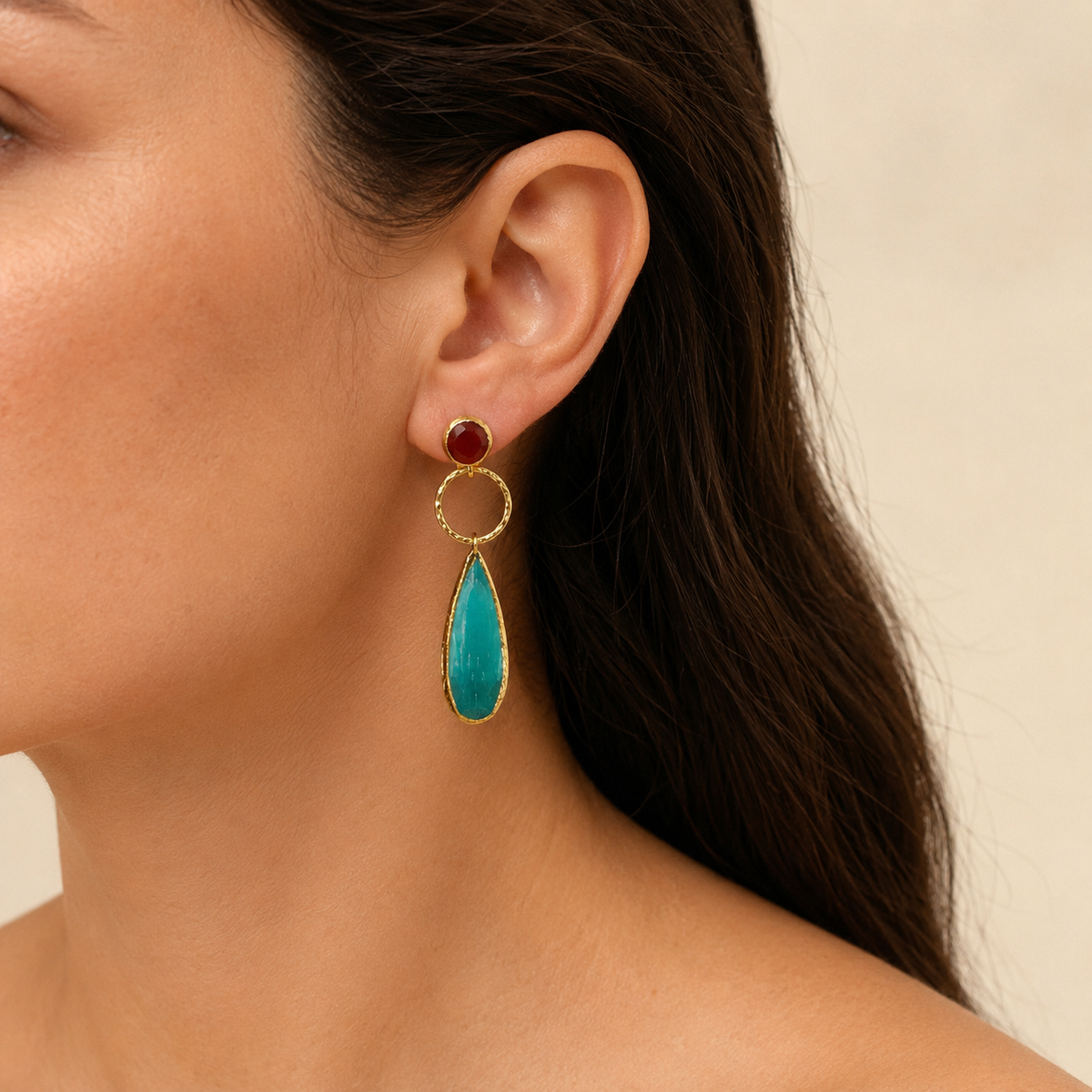 Close-up of gold-plated drop earrings with textured circular links and pine green leaf-shaped pendants.