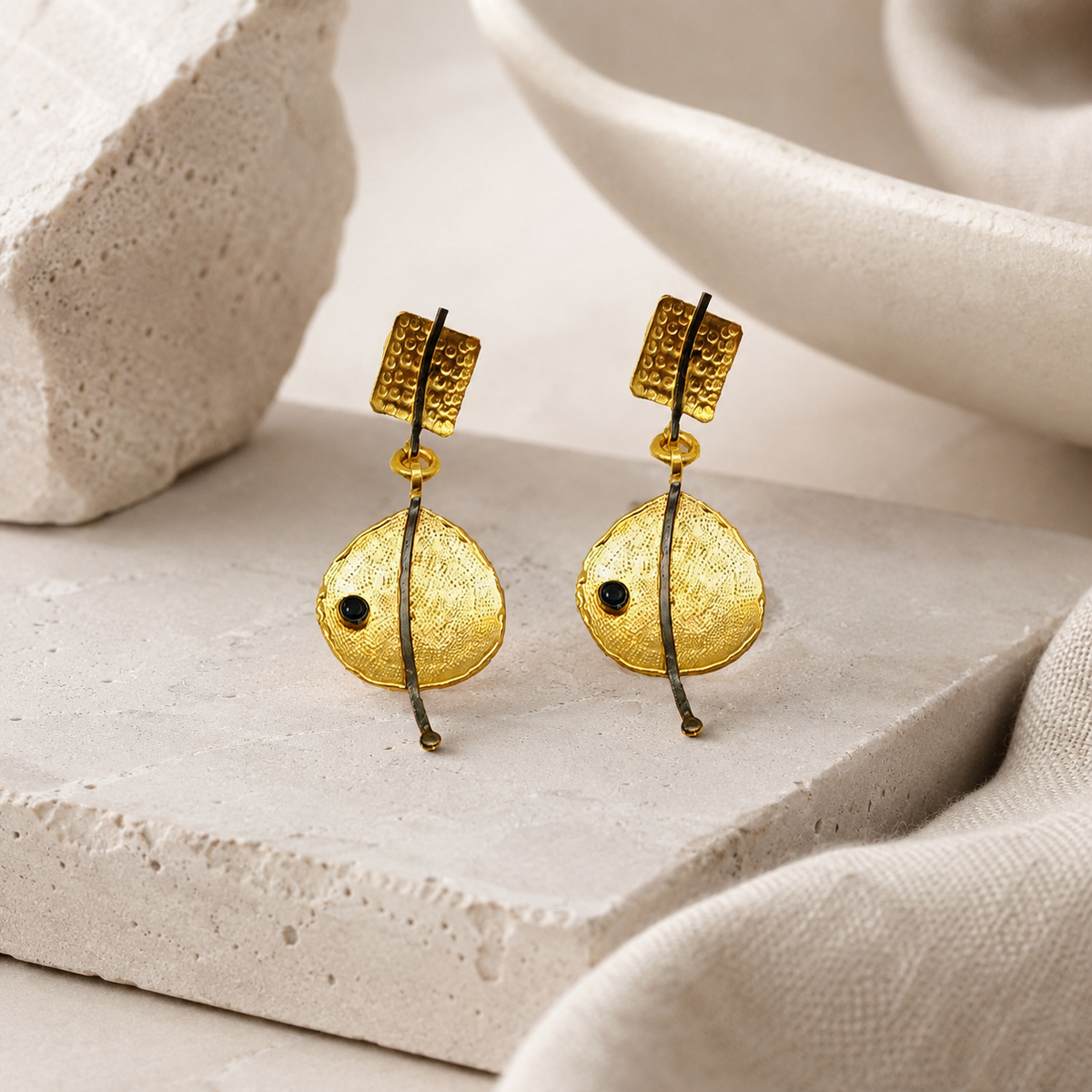 Modern drop earrings with a sculptural gold-plated finish and black accent bead.