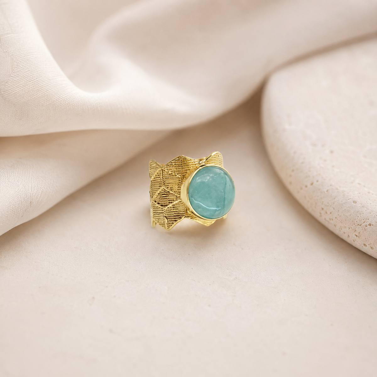A bold gold-plated ring with an aqua blue center on a white background.