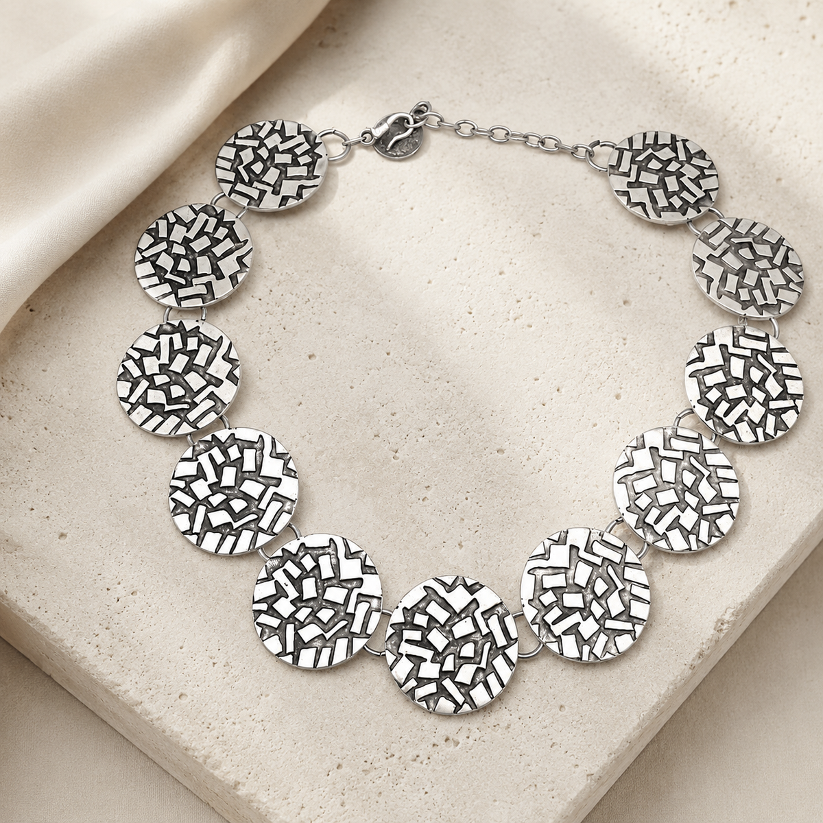 Silver statement necklace with linked round discs and a textured finish.