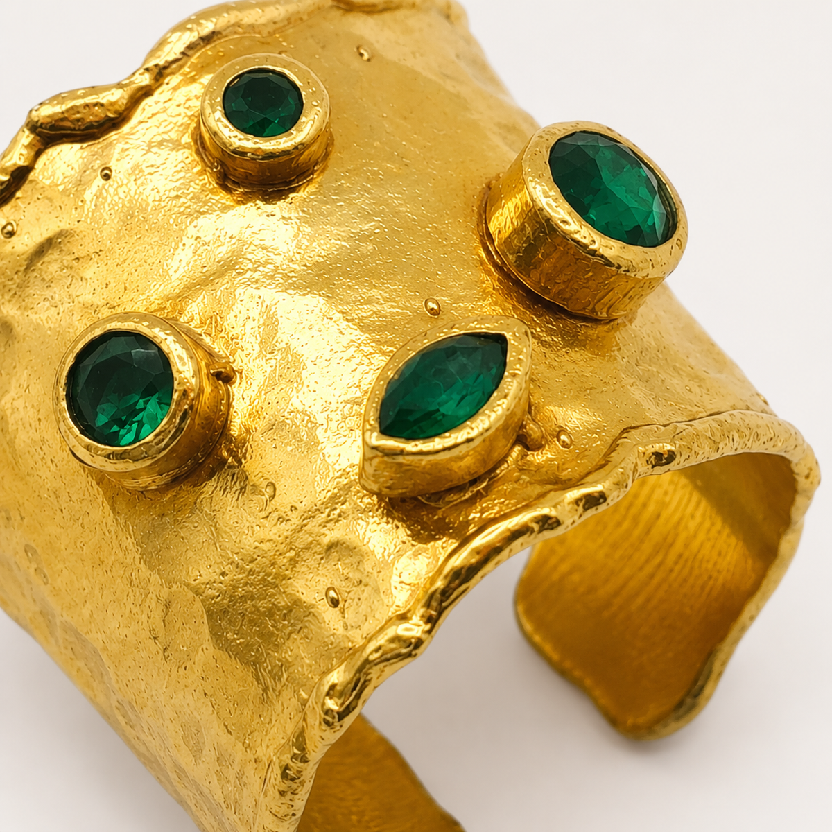 Close-up of the textured gold-plated cuff ring with emerald green stone accents.