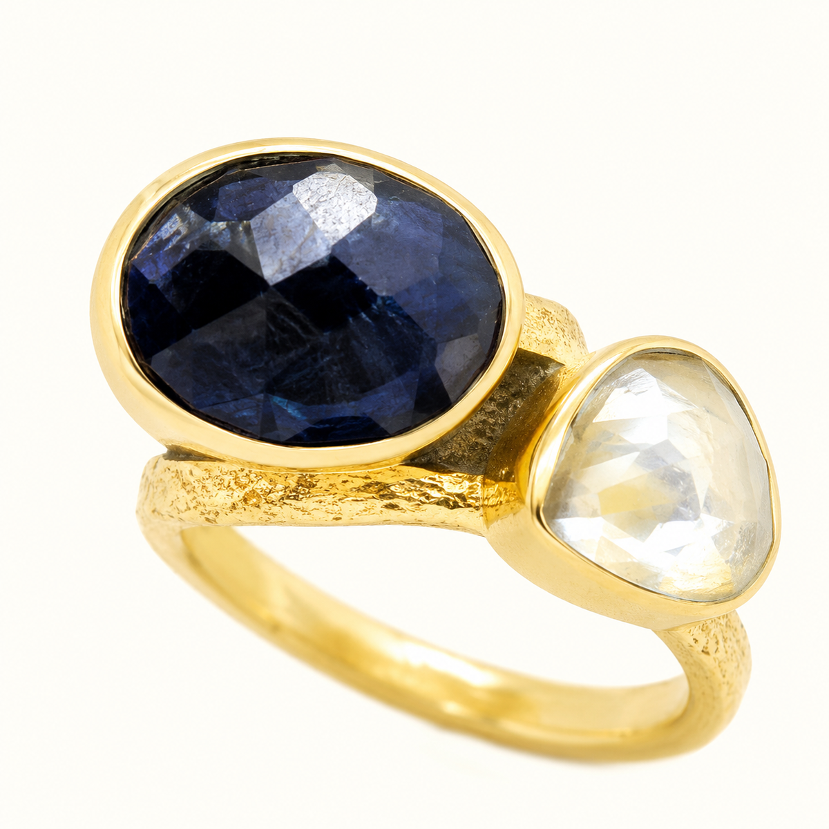 Close view of a gold ring with a faceted navy blue crystal and pearl-like accent.