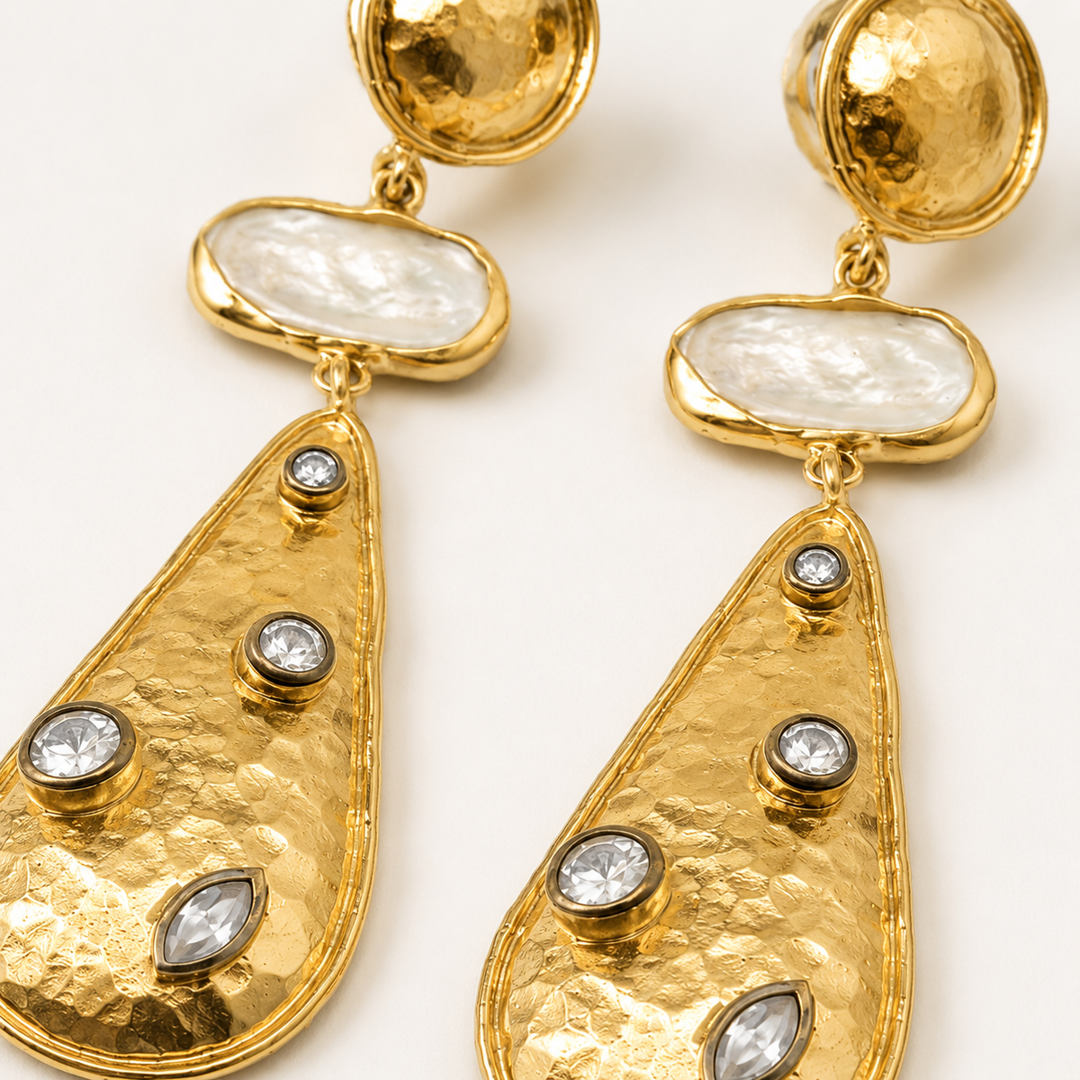 Close view of gold-plated earrings with textured surfaces and clear stone details.