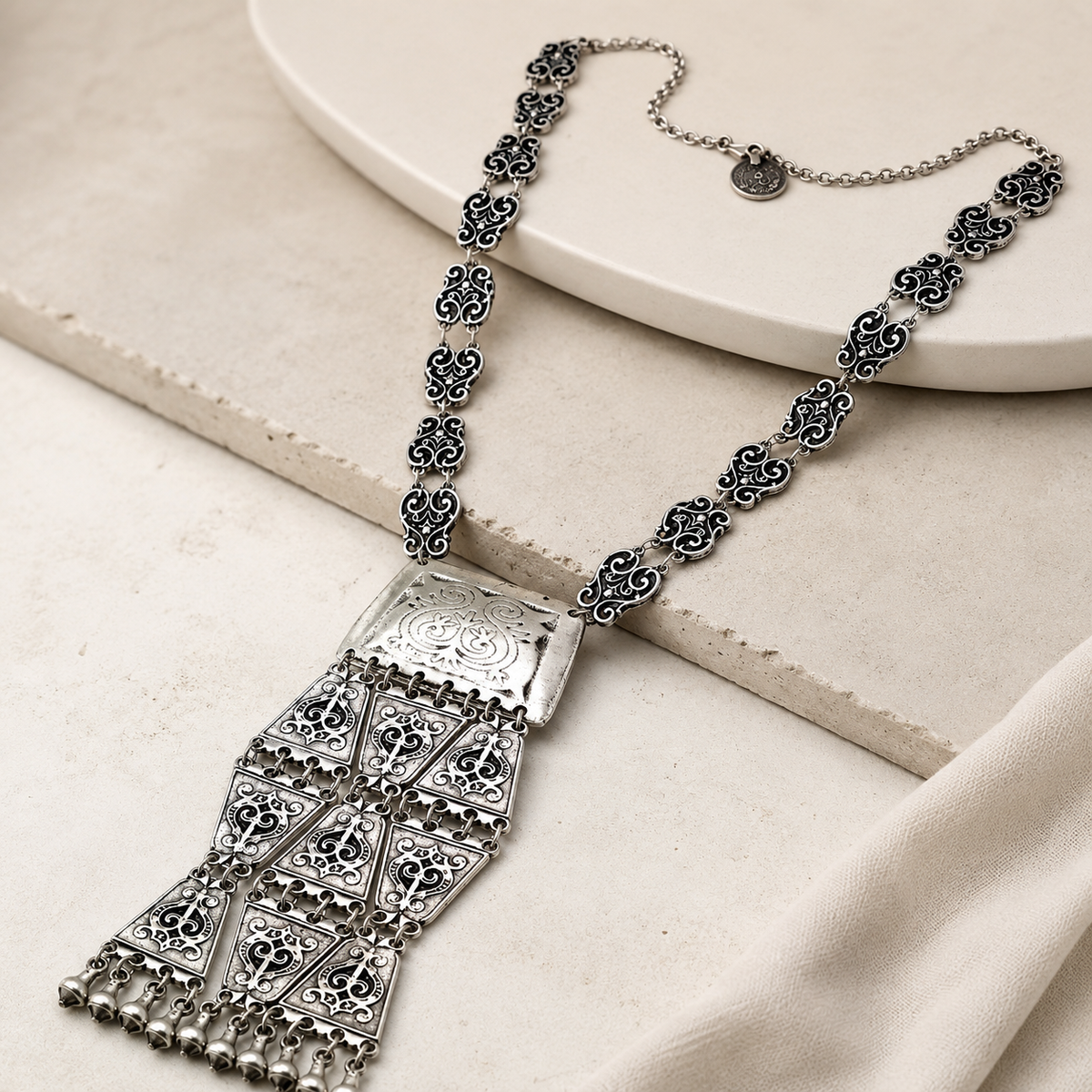 Angled view of a silver-tone triangle coin tassel necklace.