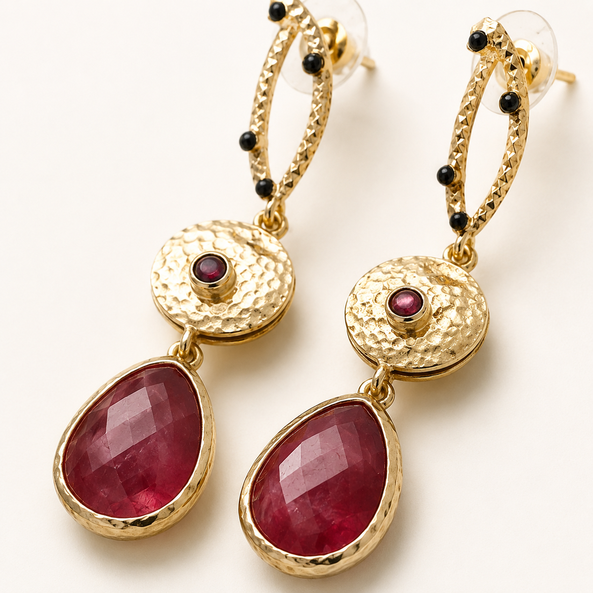 Close-up of long gold-plated statement earrings with textured details and red faceted stones.