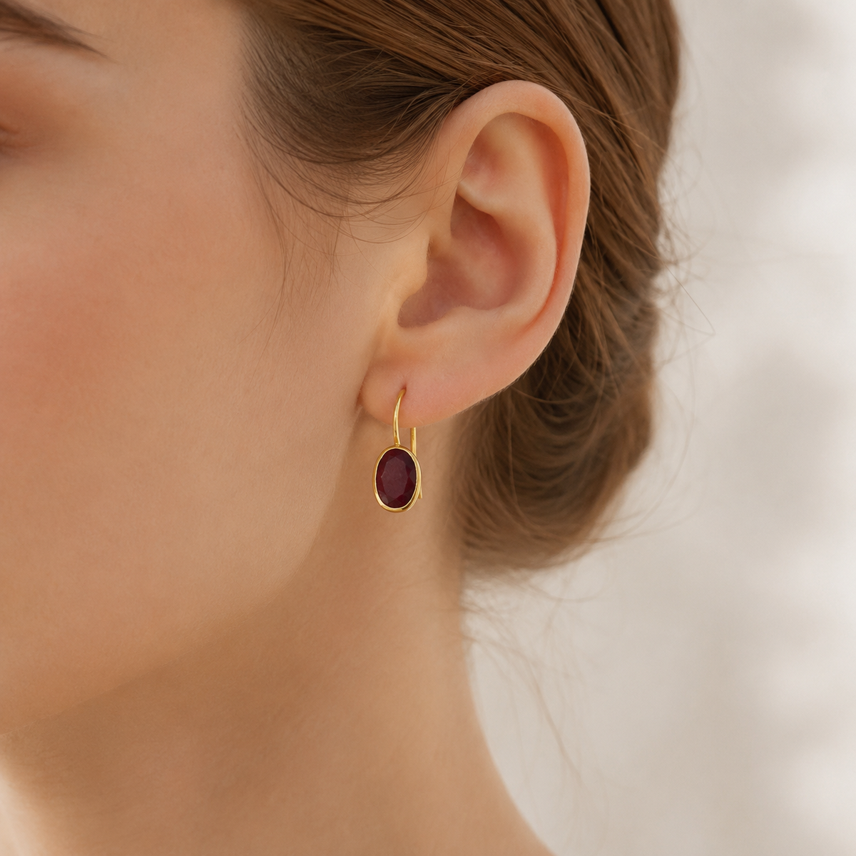 Gold-plated drop earrings with oval deep red stones shown from the front.