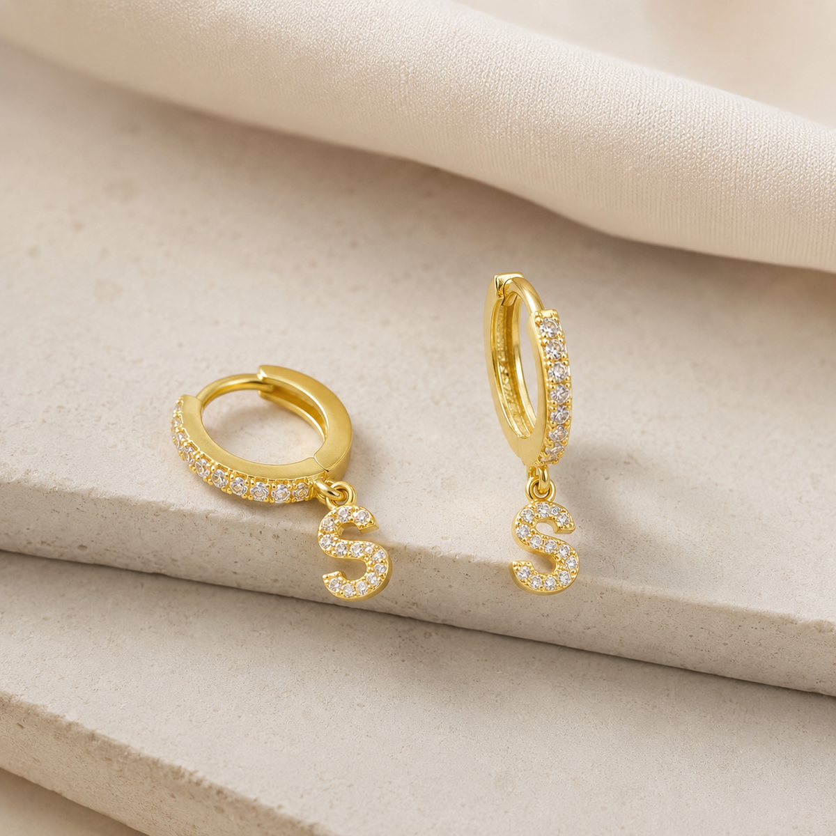 Angle view of gold-tone personalized CZ initial huggie earrings with a slim vertical bar and initial drop.