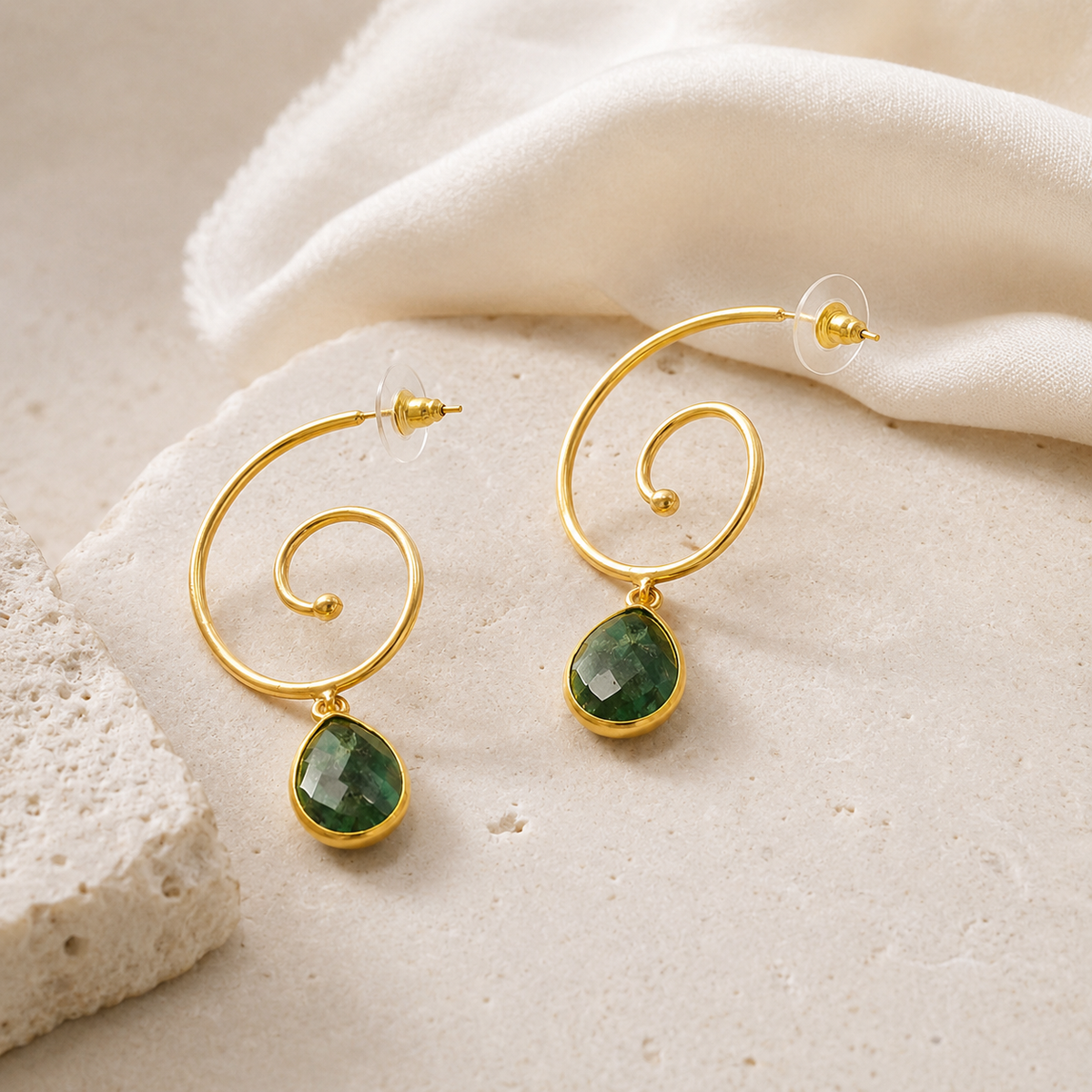 Angle view of spiral gold-plated drop earrings with green stone pendants.
