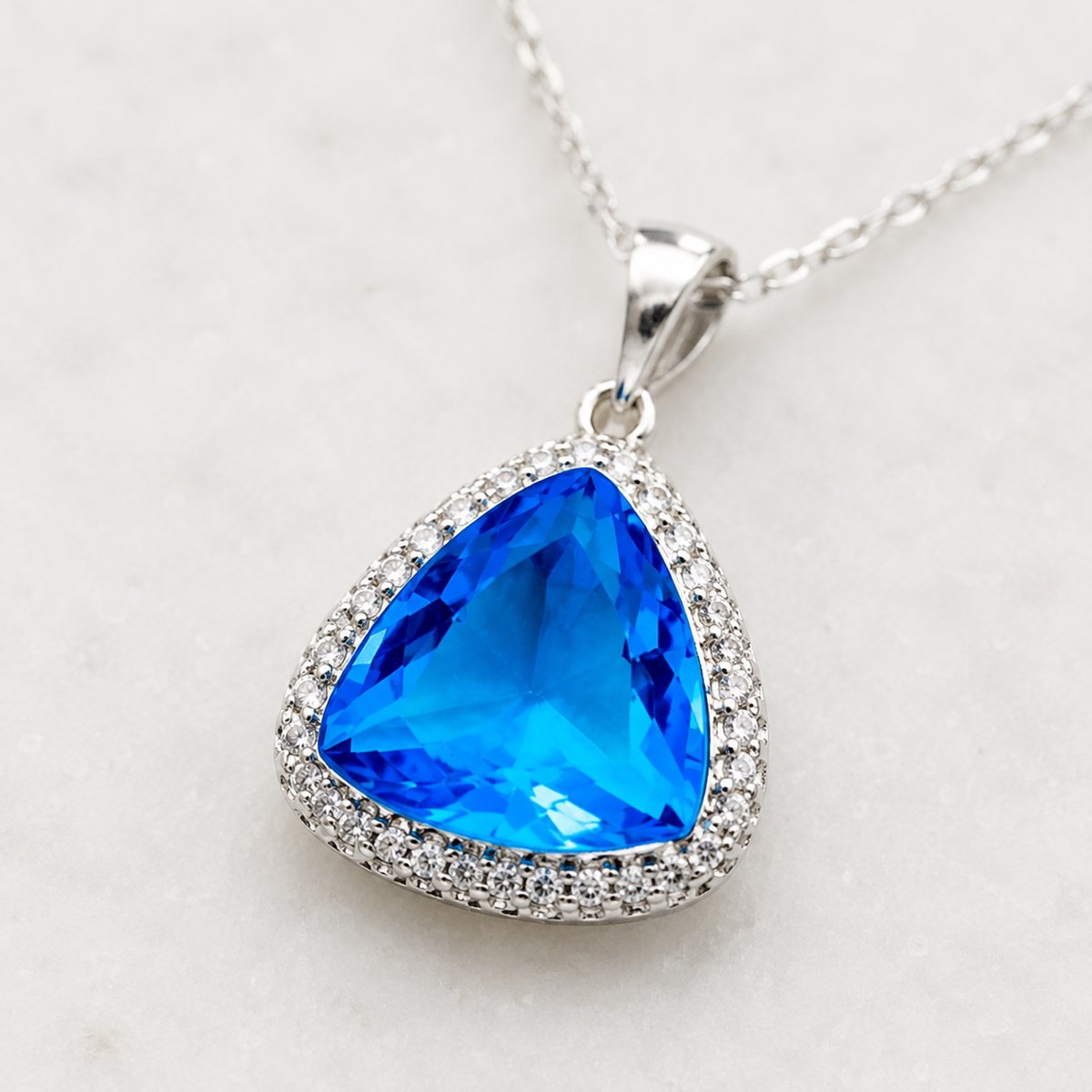 Close view of the triangle pendant necklace with a baby blue faceted stone.