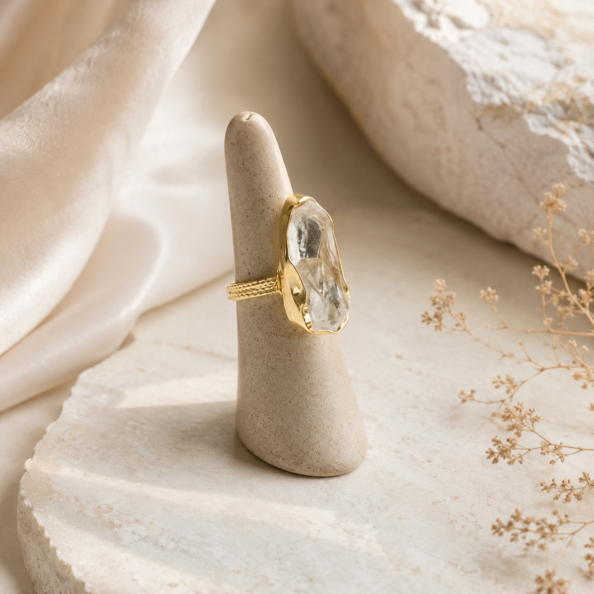 Gold-plated ring with a raw clear quartz stone on a white background.