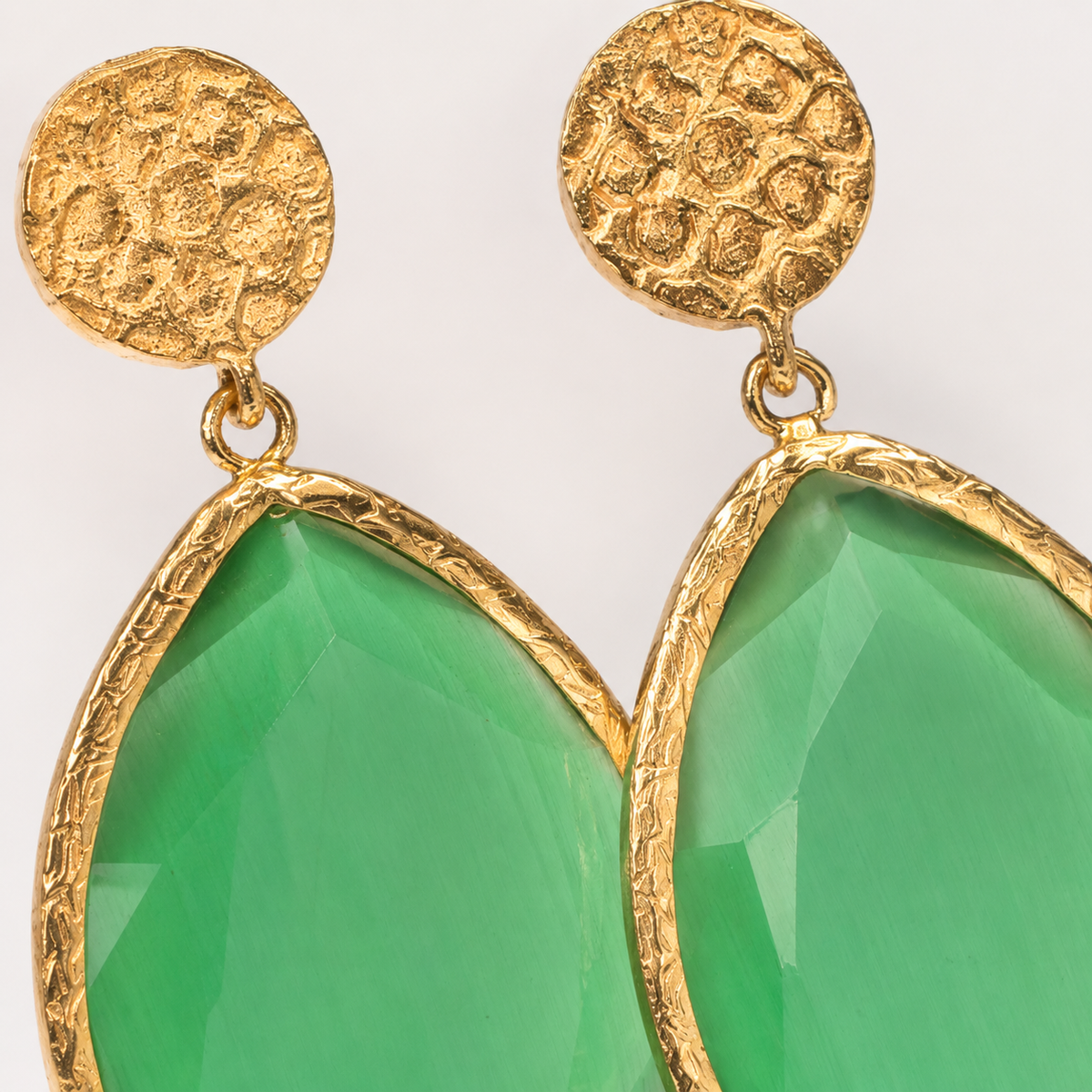 Close view of gold-plated teardrop earrings with textured round tops and green faceted drops.
