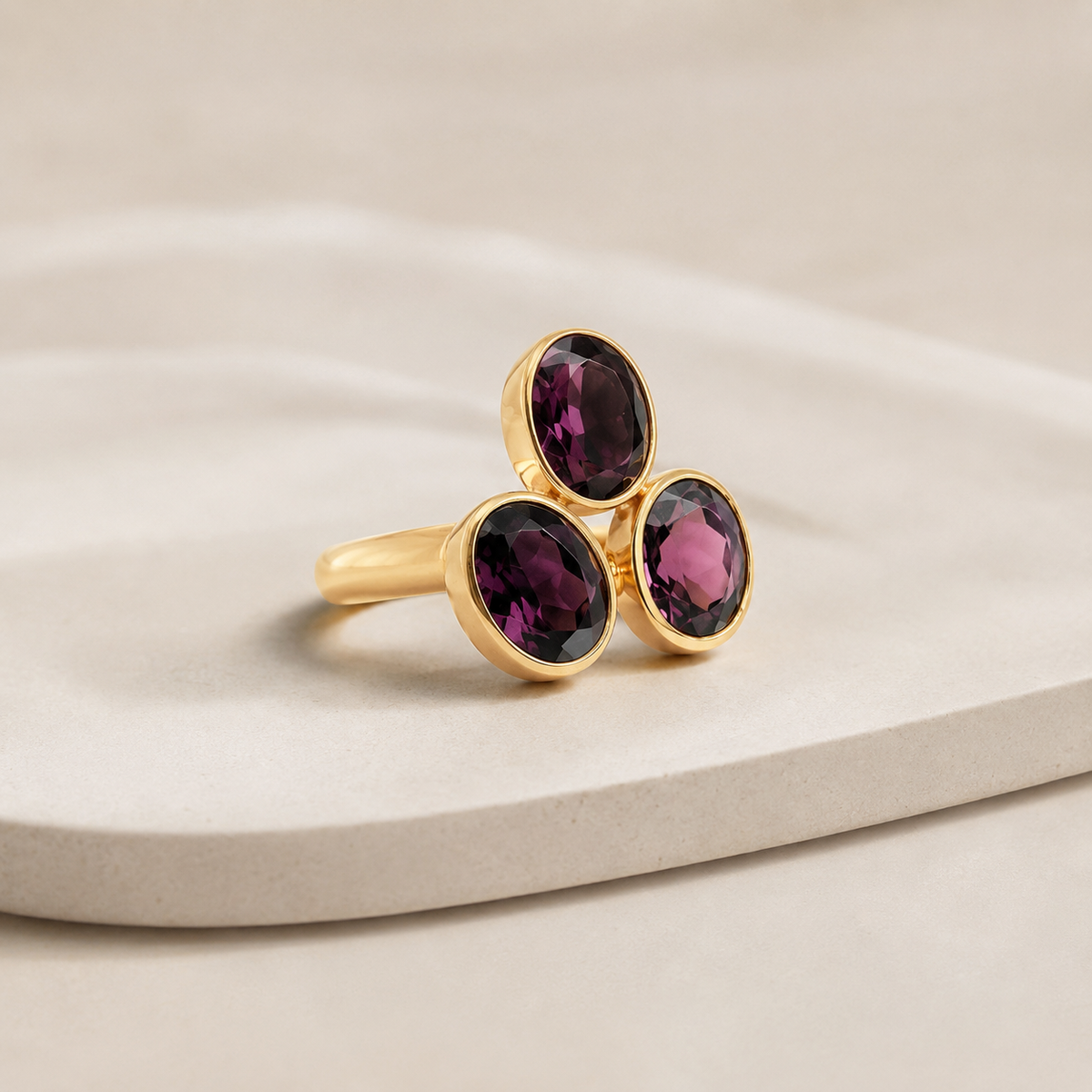 Angle view of a gold-plated ring with three oval amethyst stones.