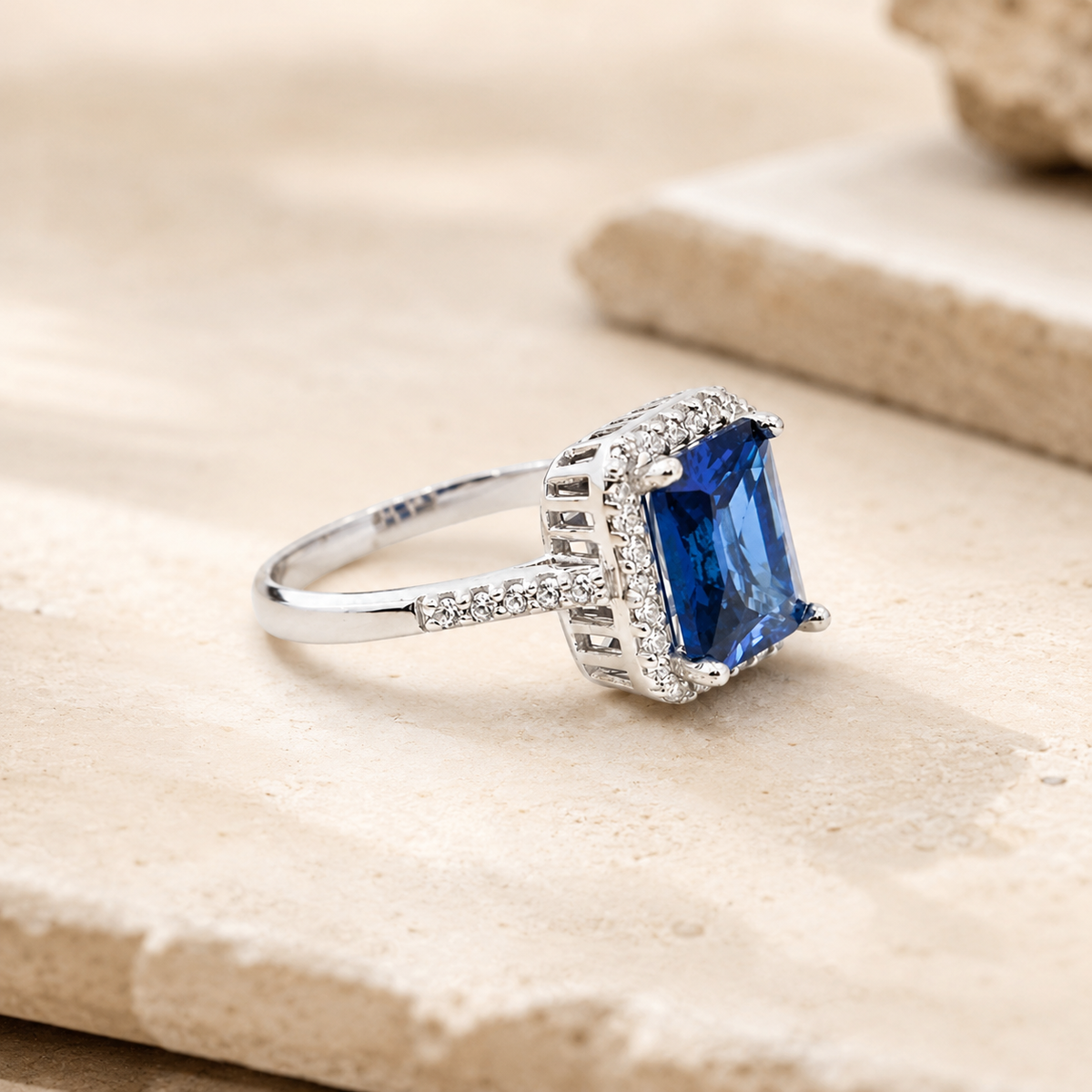 Side angle of a cushion cut blue sapphire ring in a silver-tone setting.