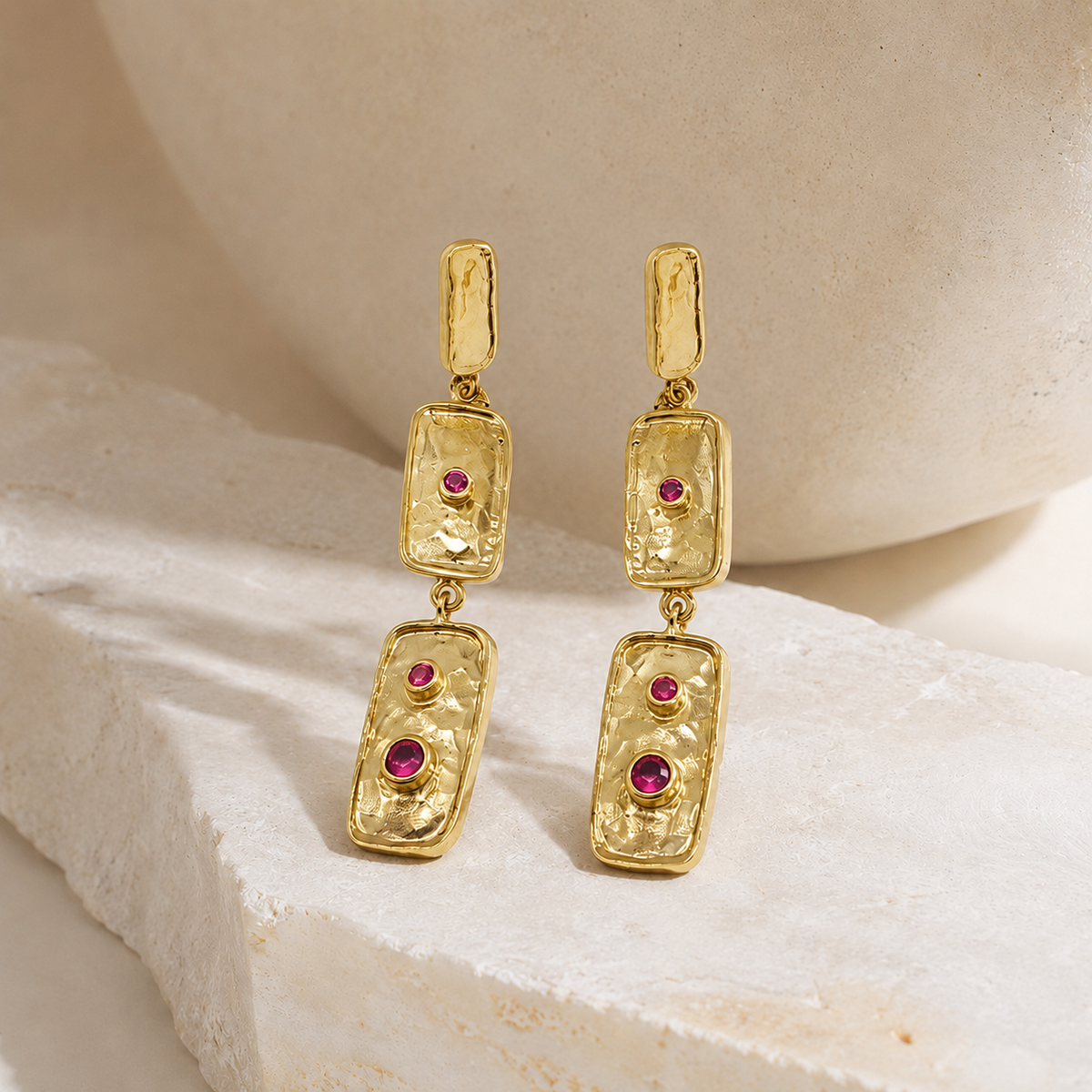 Close view of textured gold-plated rectangle earrings with pink stone accents.