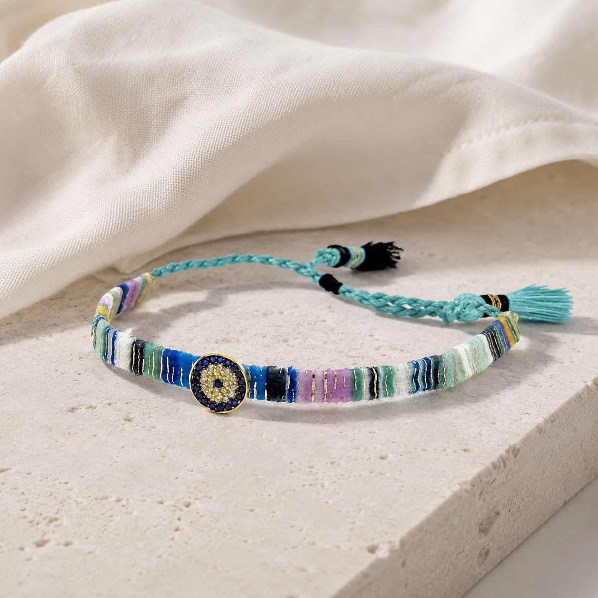 Multicolor woven bracelet with tassel ties and a jeweled evil eye detail.