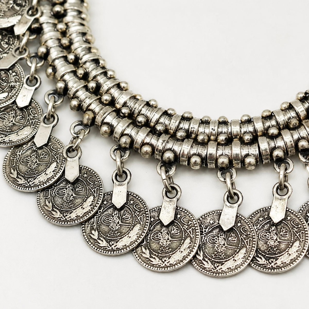 Close view of the necklace’s textured silver-tone coin details and layered rows.