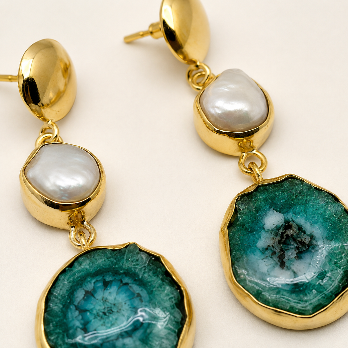 Close-up of gold-plated drop earrings with a baroque pearl and green agate detail.