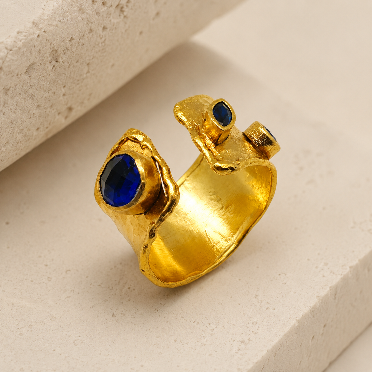 Angled view of a gold-plated open cuff ring with sapphire blue stones.