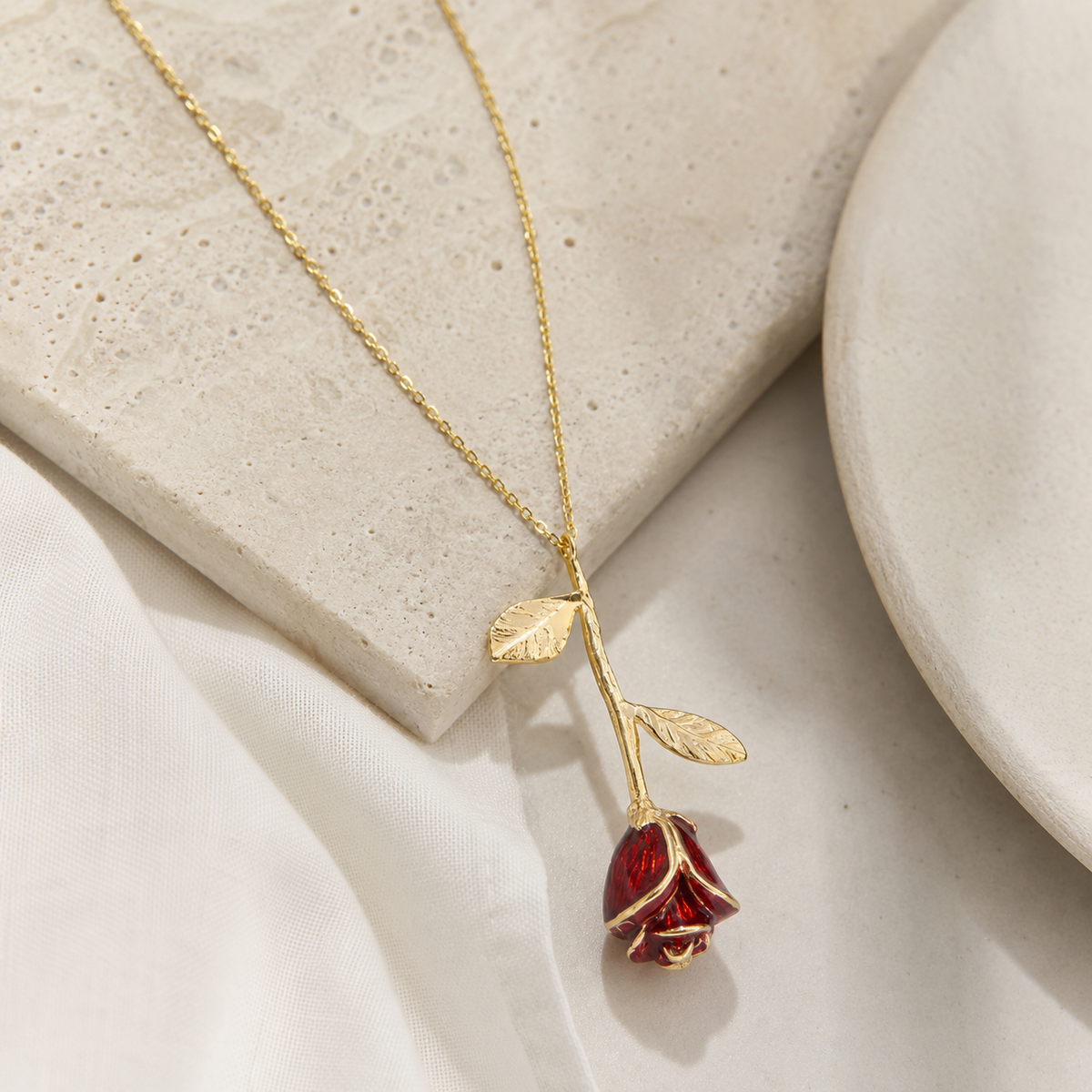 Angled view of a rose pendant necklace with red petals and leaf details.