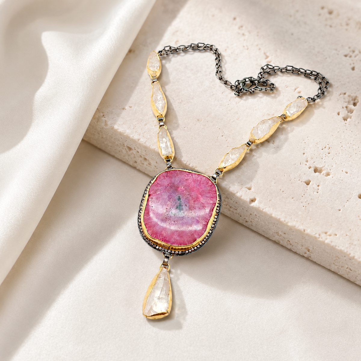 Pink solar stone necklace with a gold-tone setting and layered teardrop details.